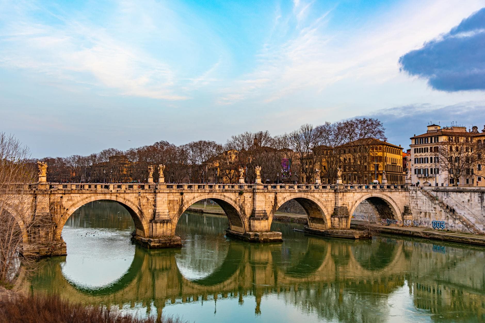 Scenic view of Ponte Sant'Angelo spanning the Tiber in Rome with reflections and vibrant sky.