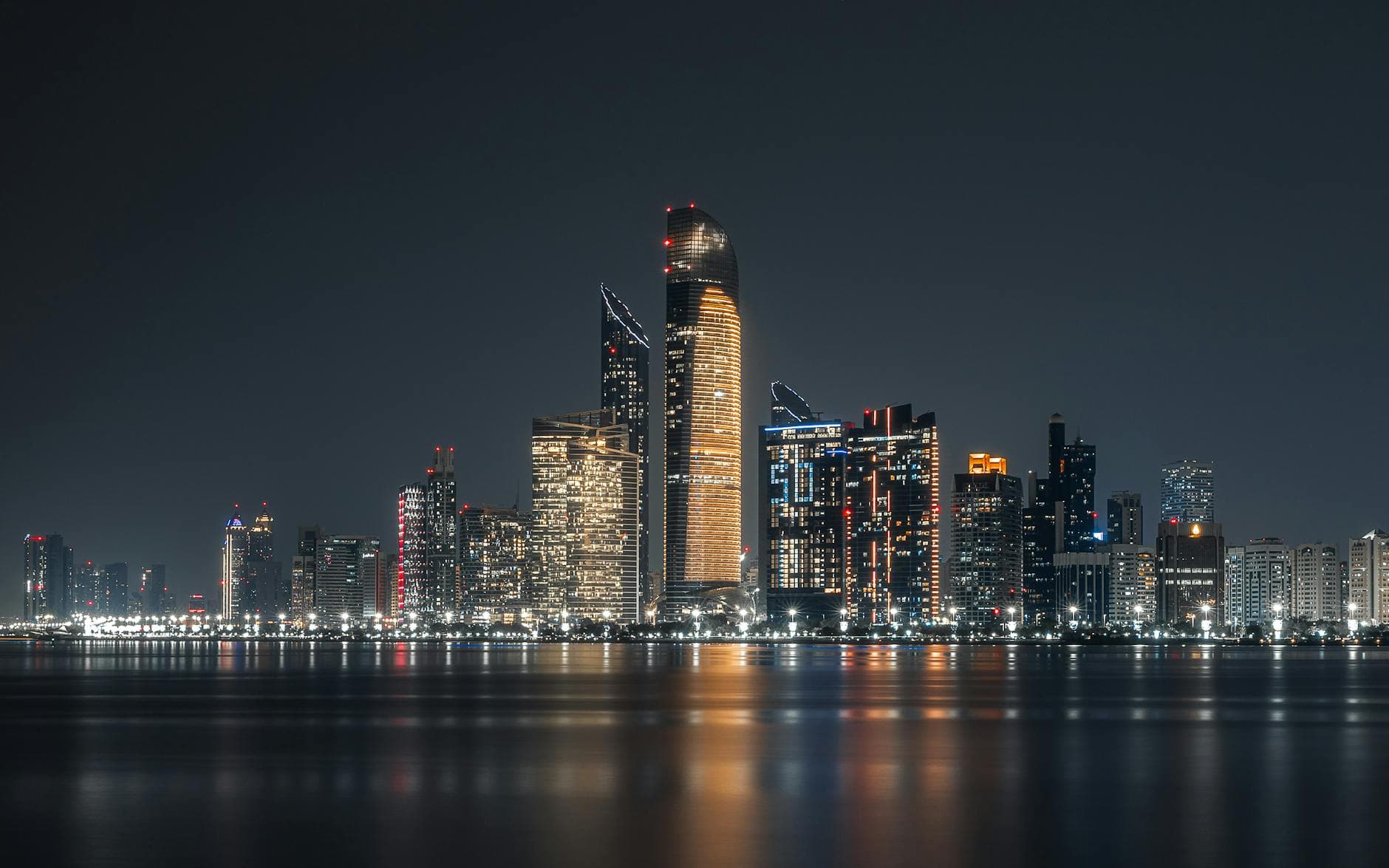 Illuminated Abu Dhabi skyline reflecting on waterfront at night.