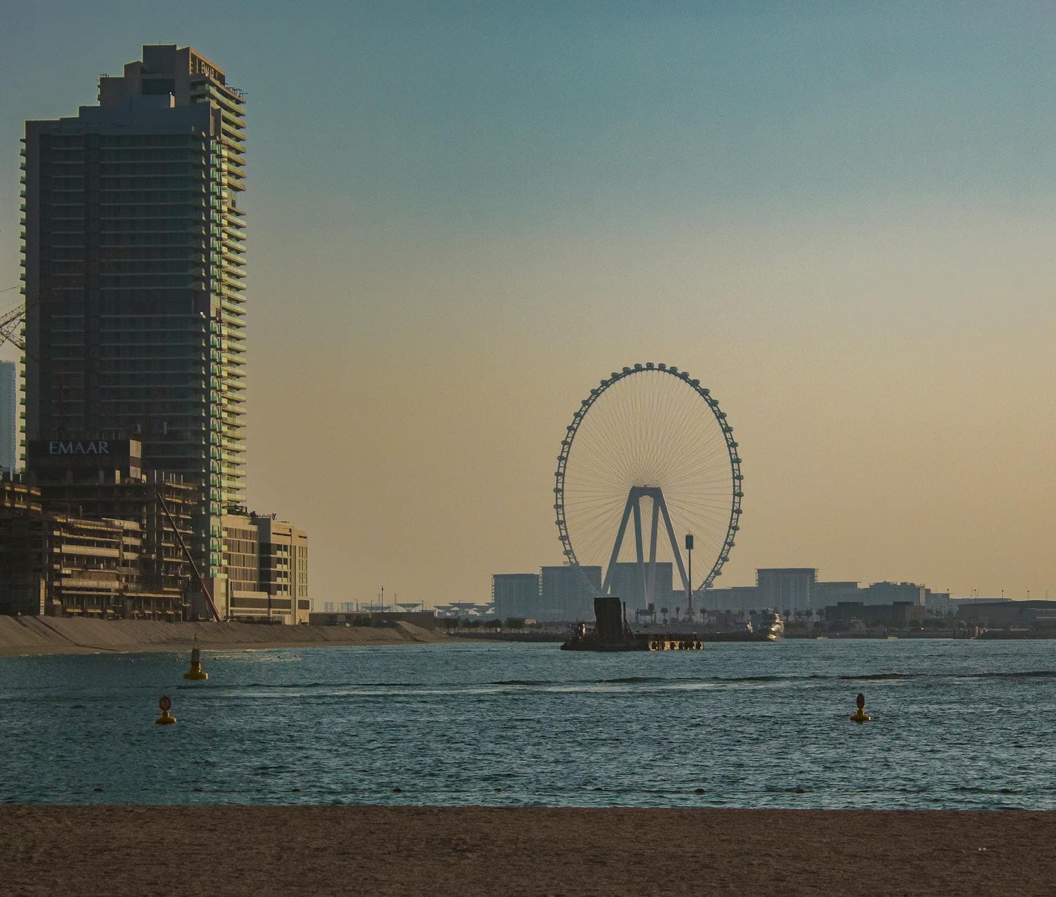 Capture of Dubai's skyline featuring the Ain Dubai Ferris Wheel during sunset over water.