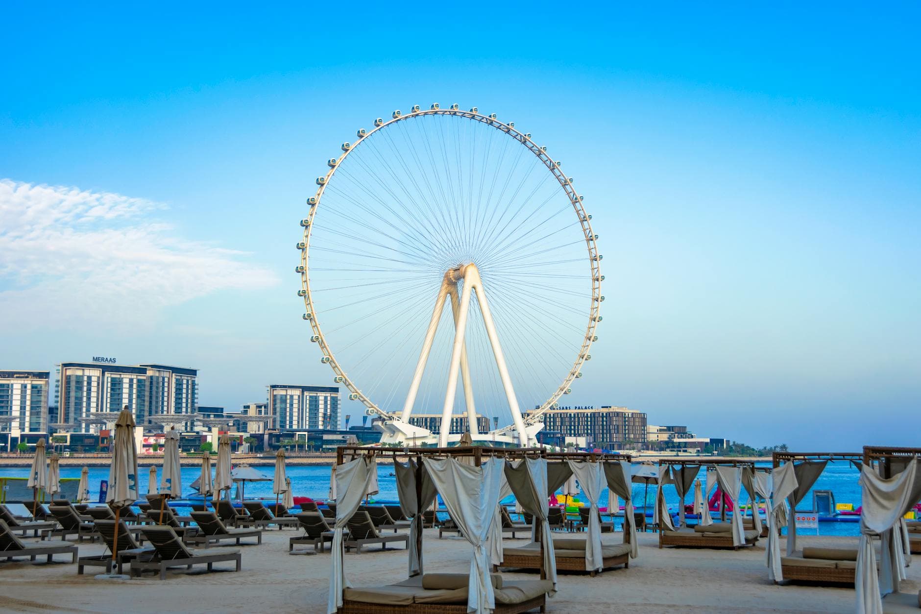 Experience a vibrant view of Dubai's Ferris Wheel against a clear blue sky at Jumeirah Beach, perfect for a summer vacation.