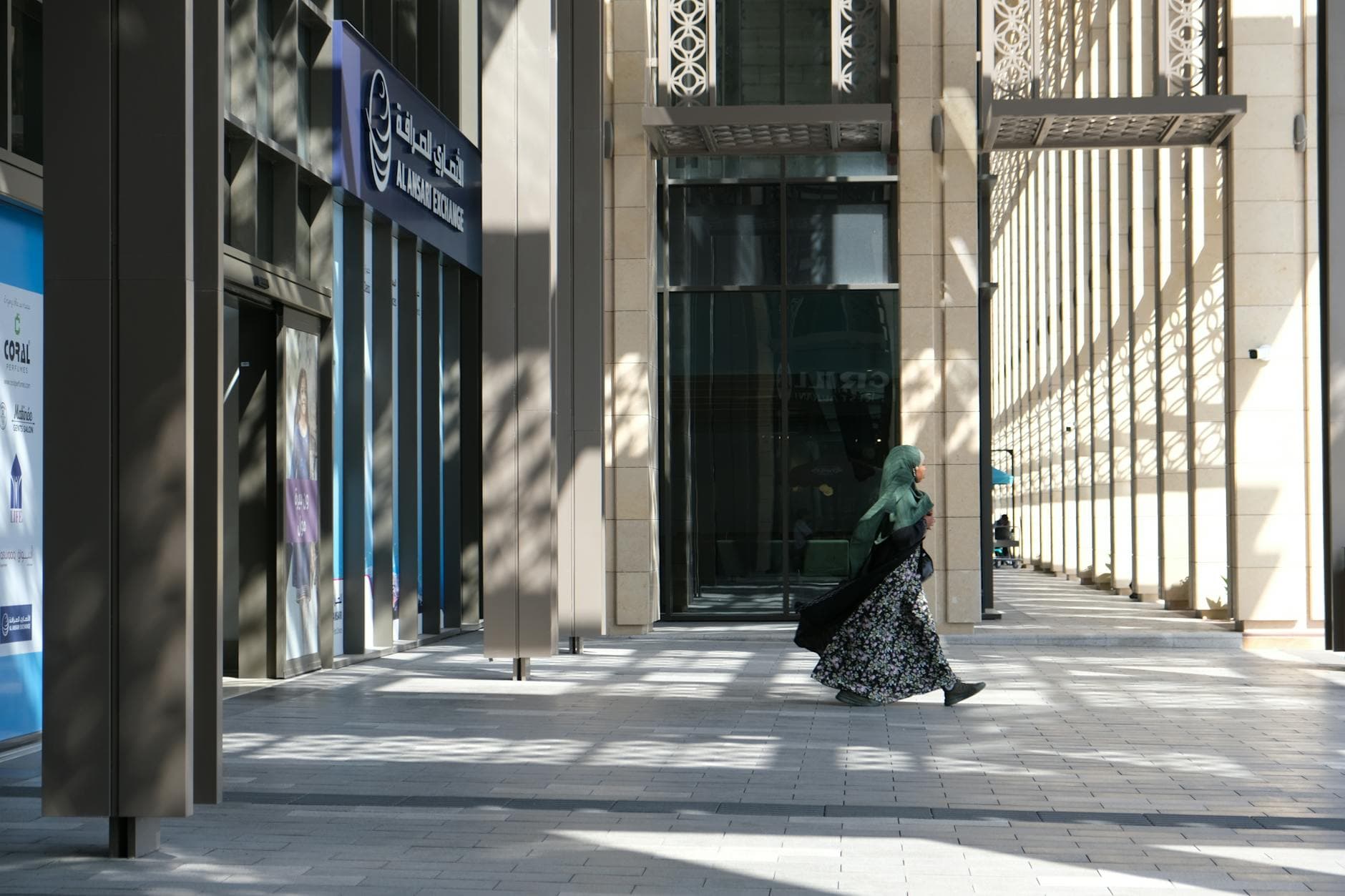 A woman in traditional attire walks in front of the Al Ansari Exchange building in downtown Dubai, UAE.
