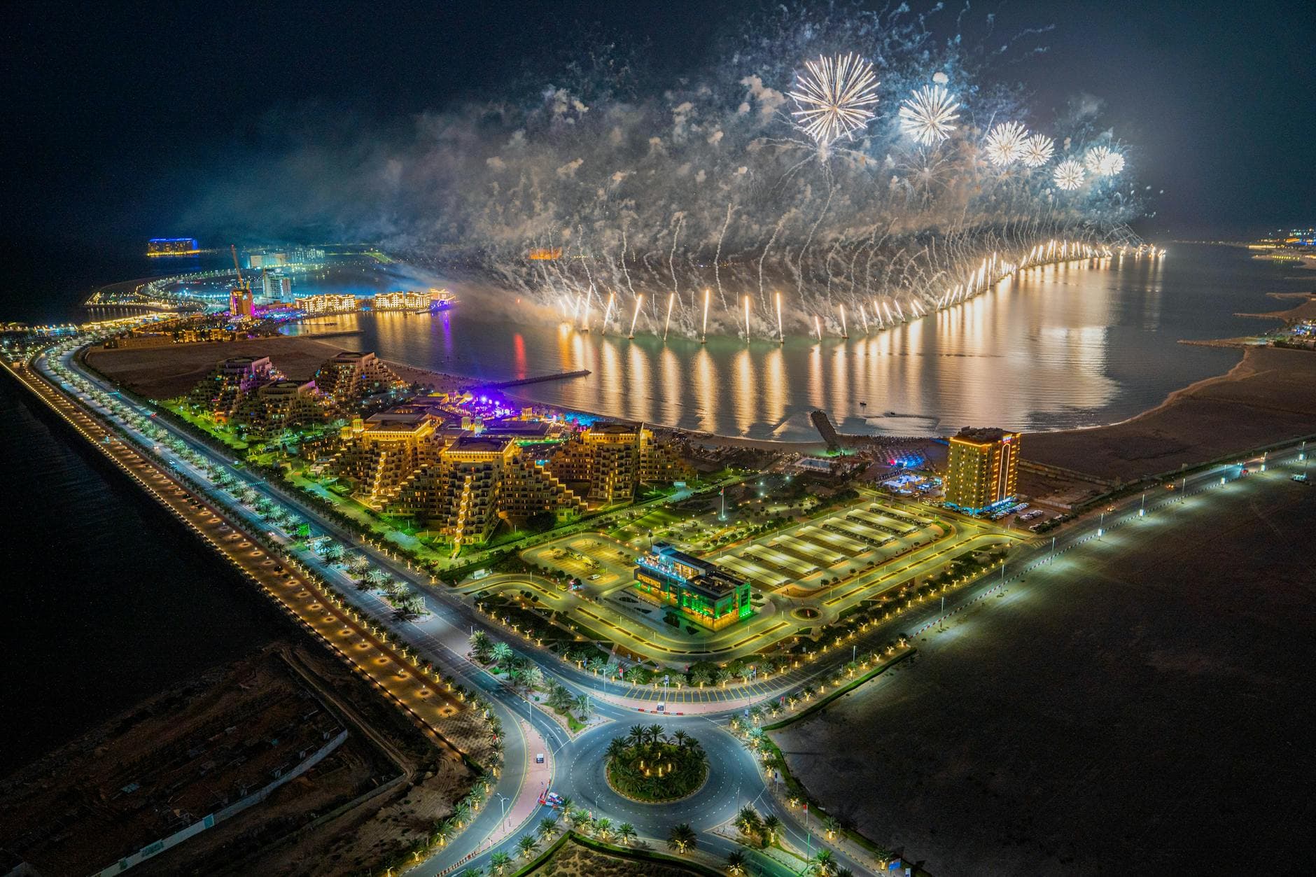 Aerial view of a vibrant fireworks display over Al Marjan Island, Ras al Khaimah, UAE at night.