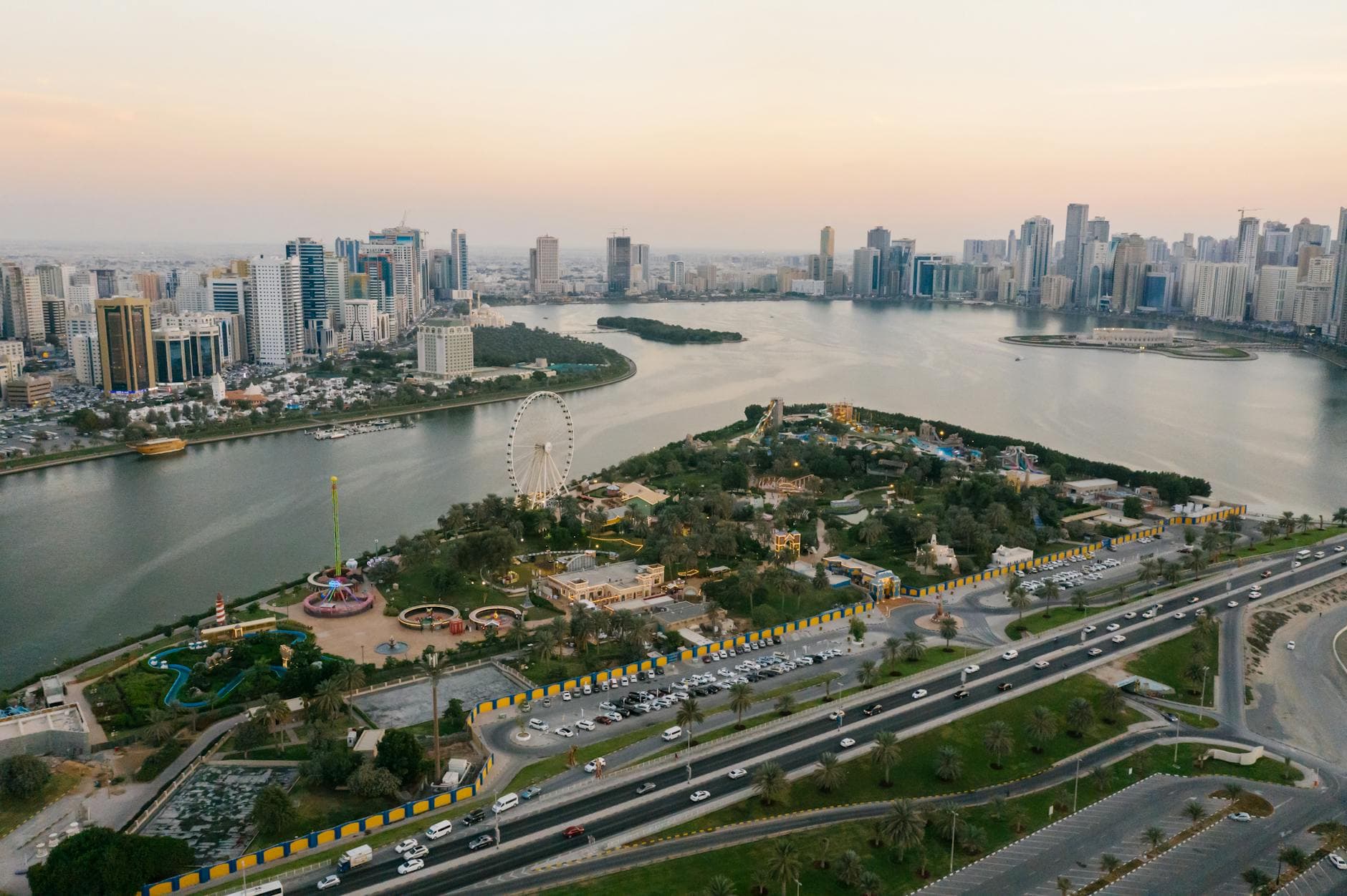 A stunning aerial shot of Sharjah cityscape featuring parks, landmarks, and coastline at sunset.