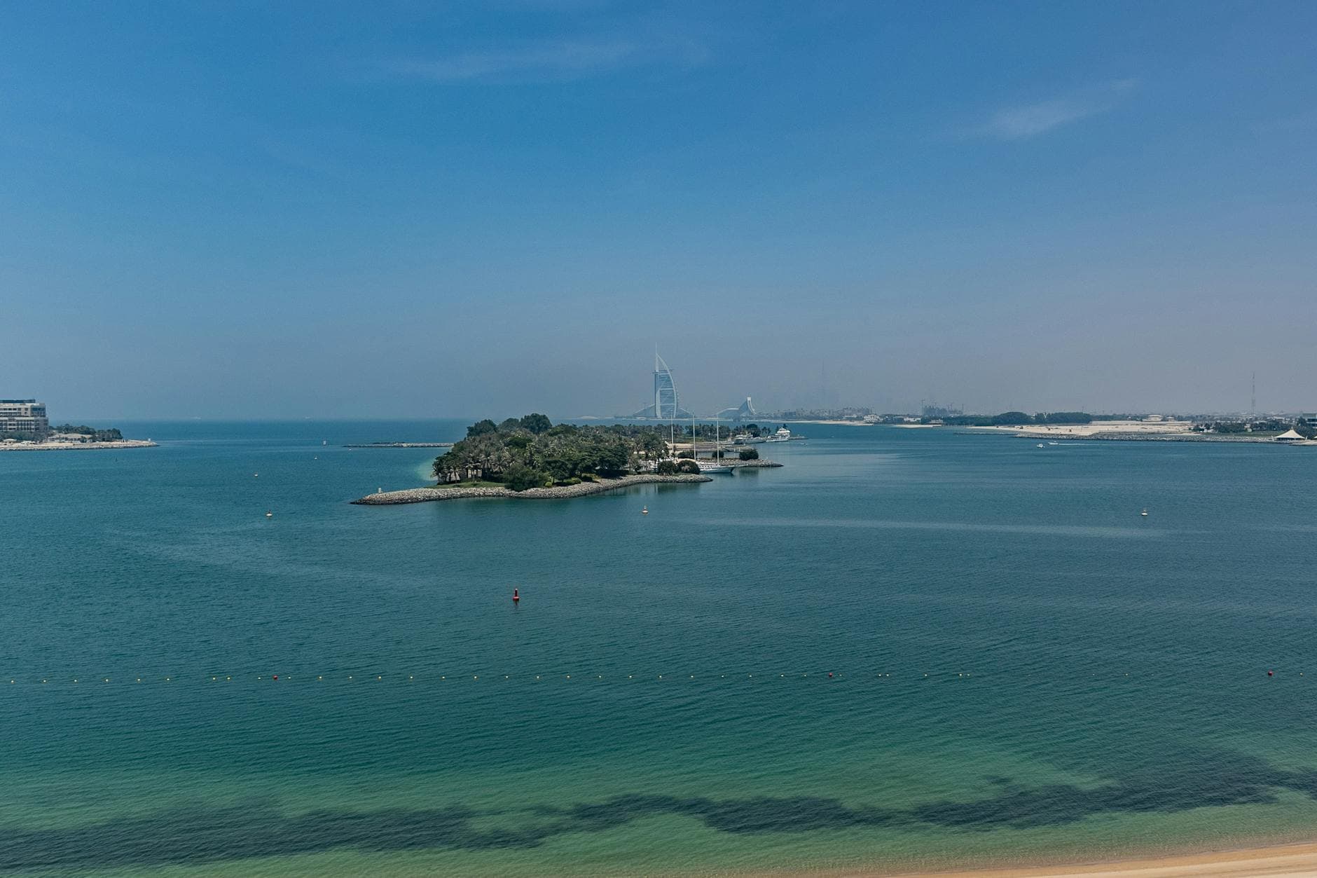 Sweeping view of Burj Al Arab against clear blue sky and tranquil sea along Dubai's coast.