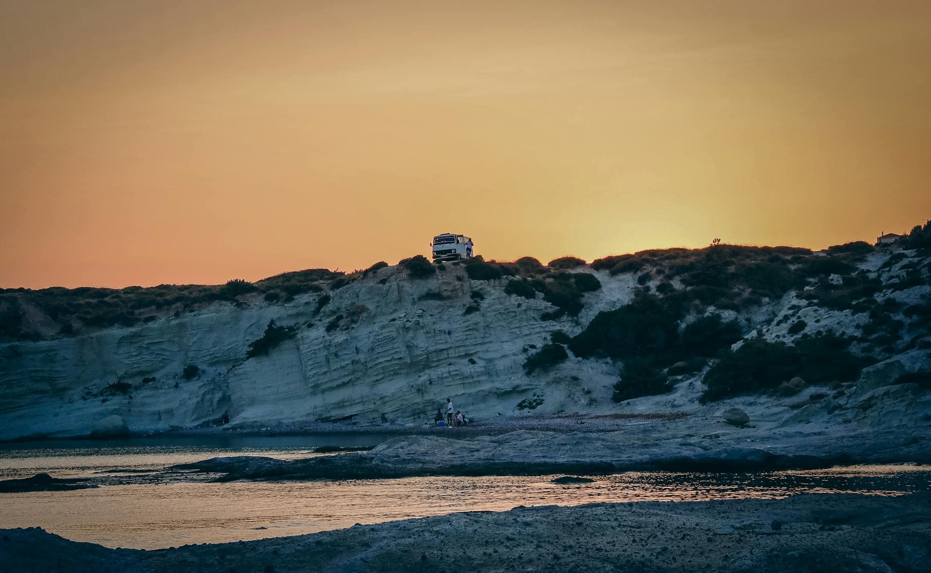 Tranquil sunset view of cliffs and beach in Alaçatı, Turkey, with vehicle on hill.