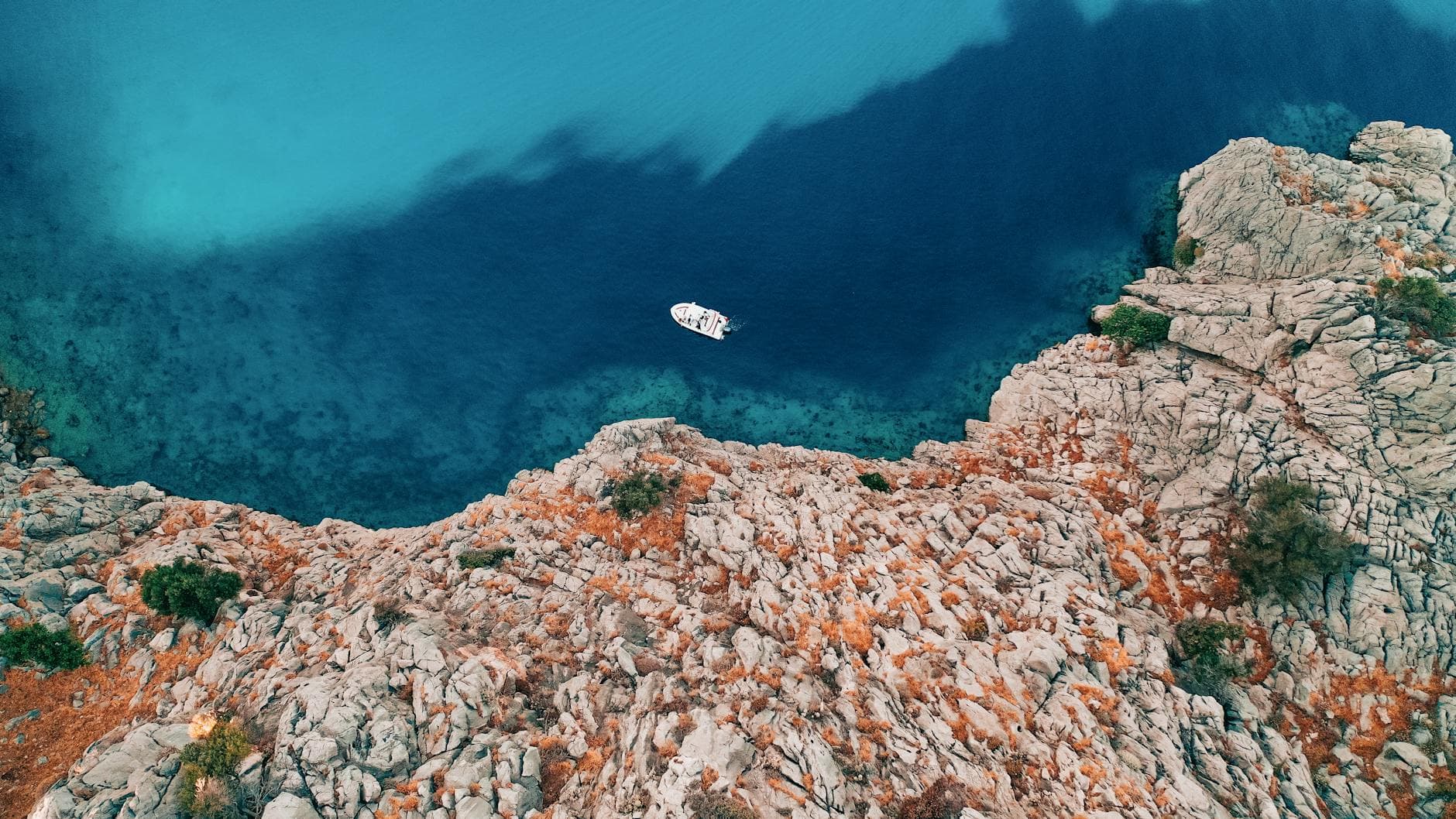 Aerial shot of a boat near rocky coastline in Alaçatı, İzmir. Scenic view of turquoise sea waters.