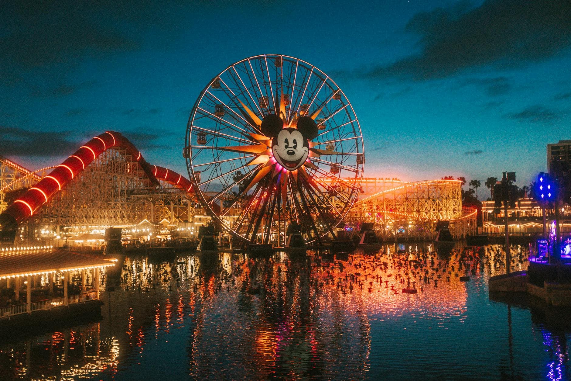 Stunning view of a brightly lit Ferris wheel at a theme park during sunset, reflecting on the water.