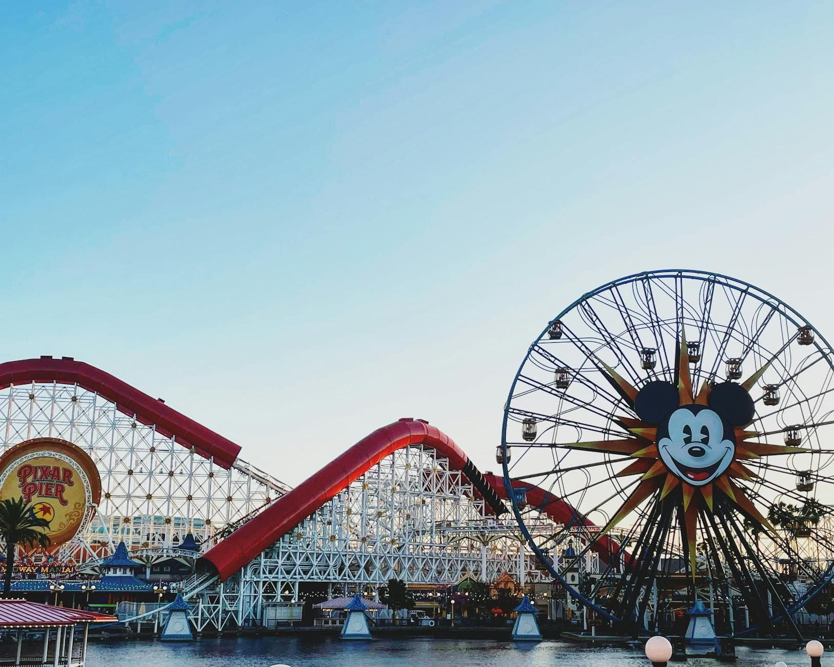 Vibrant image of a roller coaster and Mickey Mouse Ferris wheel at a theme park.