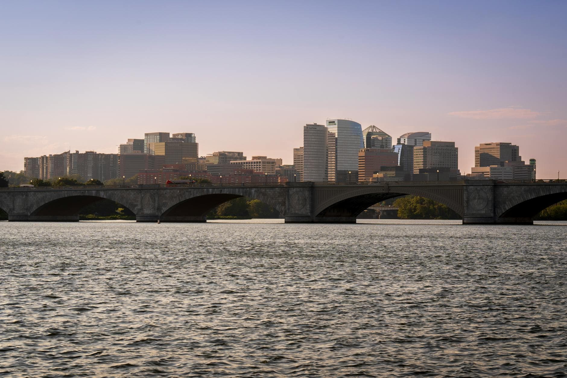 View of Arlington Memorial Bridge with modern skyline and calm river under twilight sky.