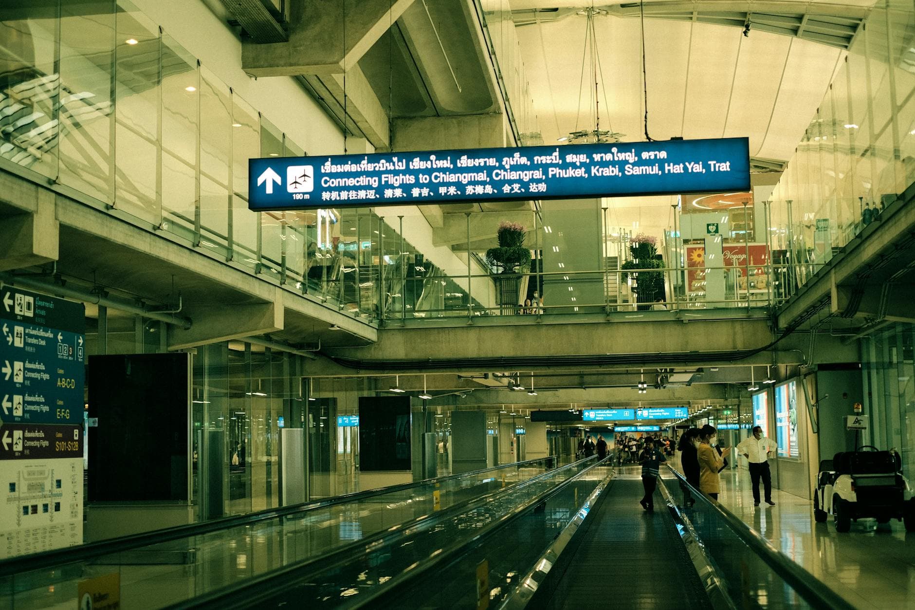 View of Suvarnabhumi Airport interior with moving walkway and signs for connecting flights.