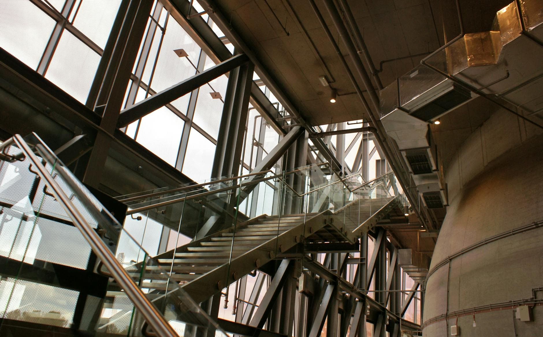 A modern industrial staircase with glass railings in a spacious industrial building interior.