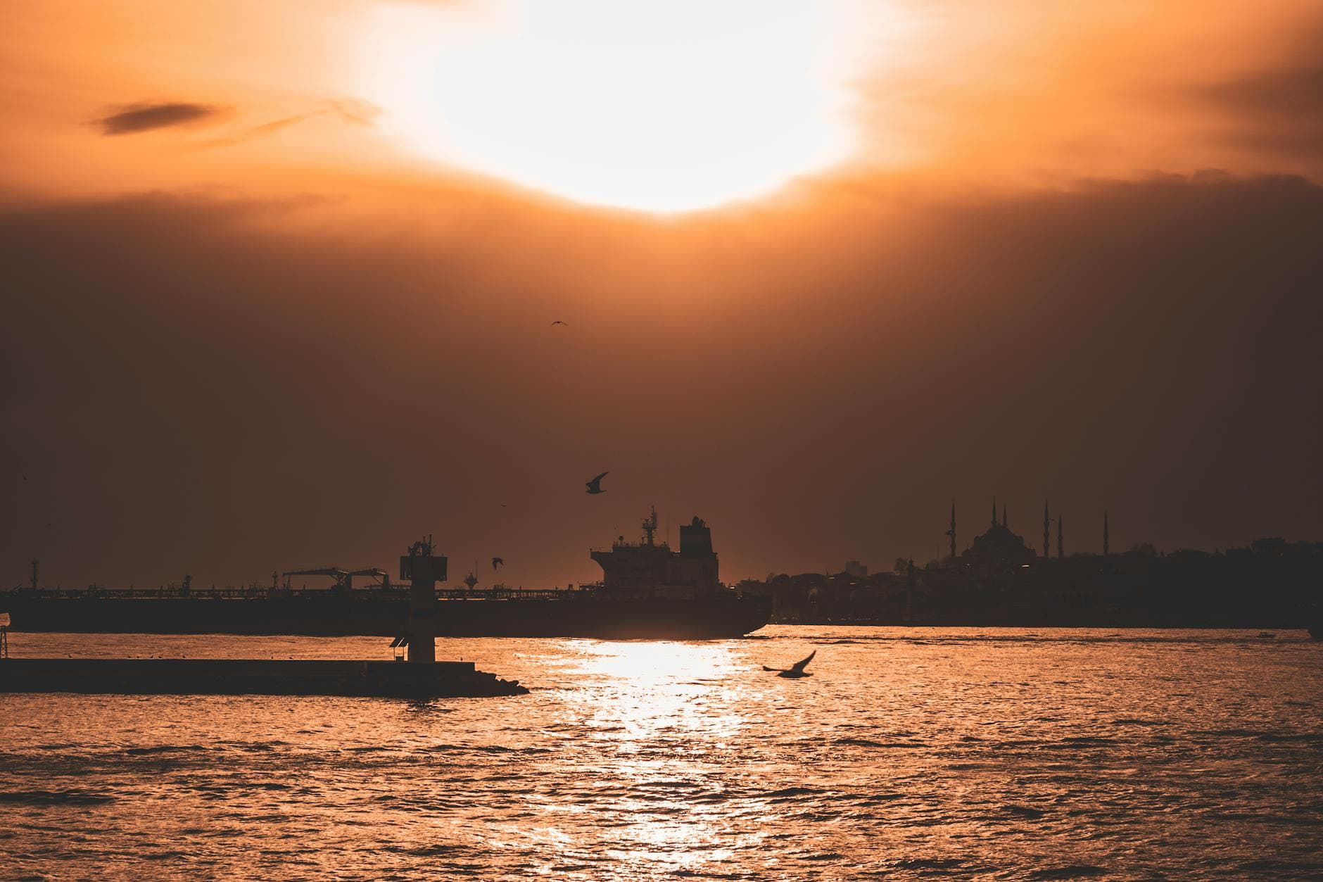 Dramatic sunset over İstanbul waterfront with silhouettes of cityscape, watercraft, and seagulls.