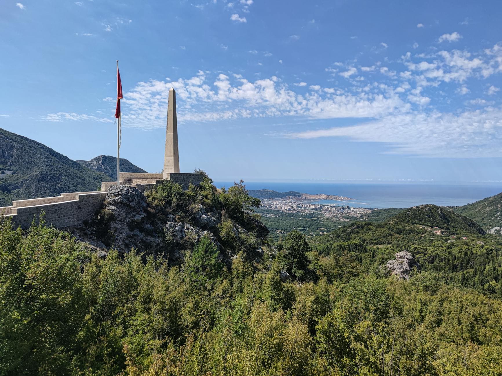 Scenic view of Bar, Montenegro from a mountain vantage point with a monument and ocean backdrop.