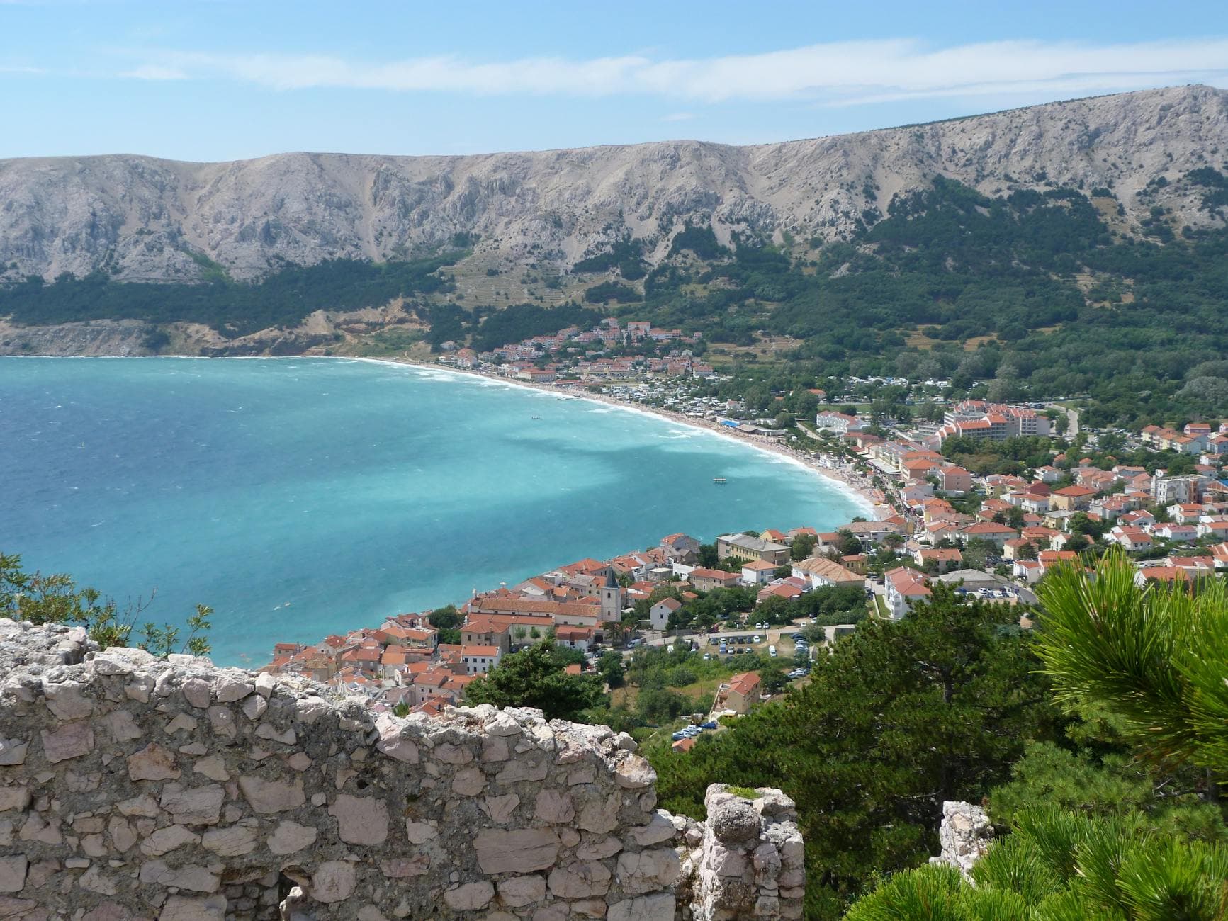 A stunning aerial view of Baška on Krk Island with turquoise waters and mountain backdrop.