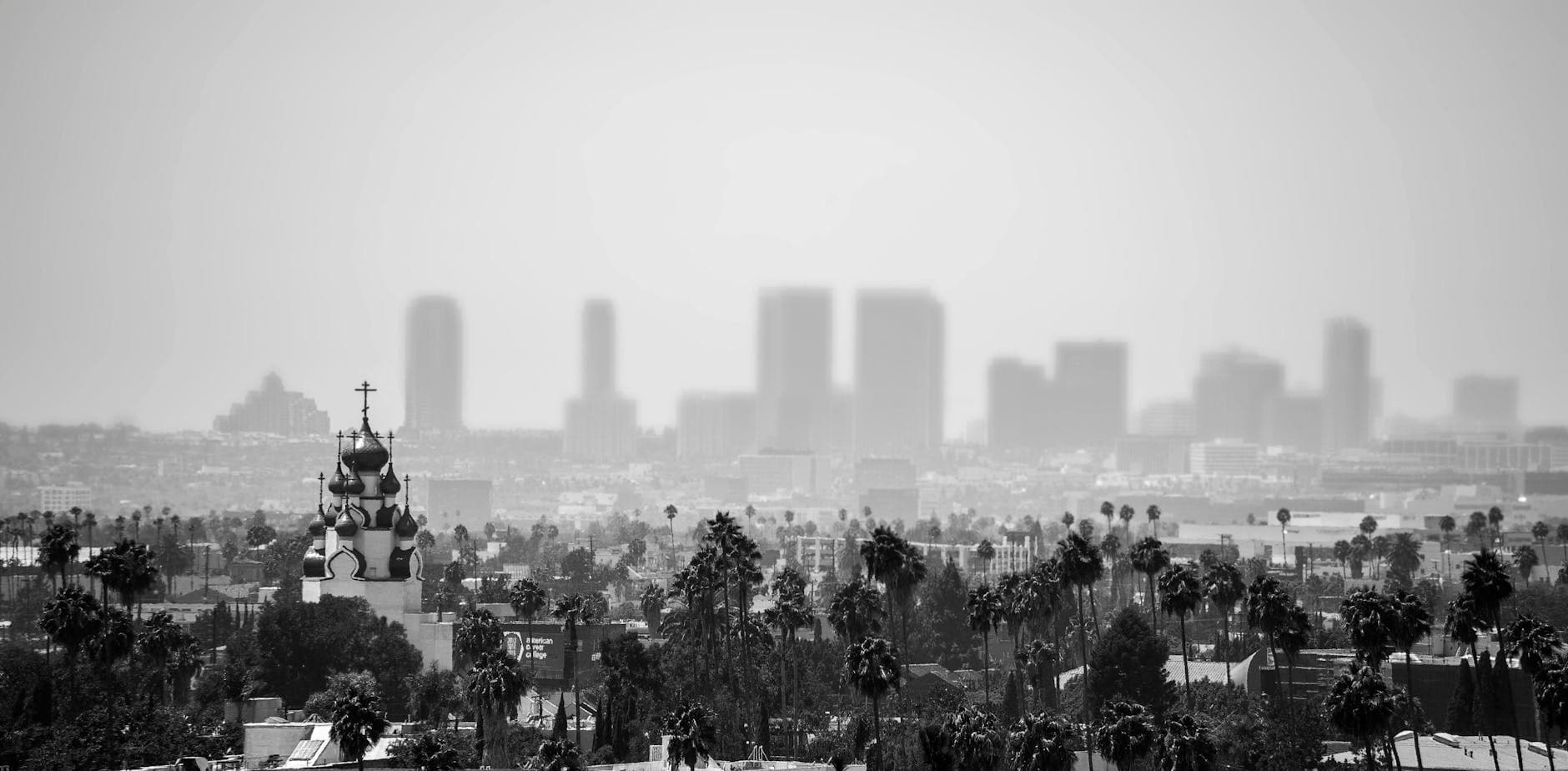 Black and white view of a historic church with Los Angeles skyline enveloped in fog and smog.