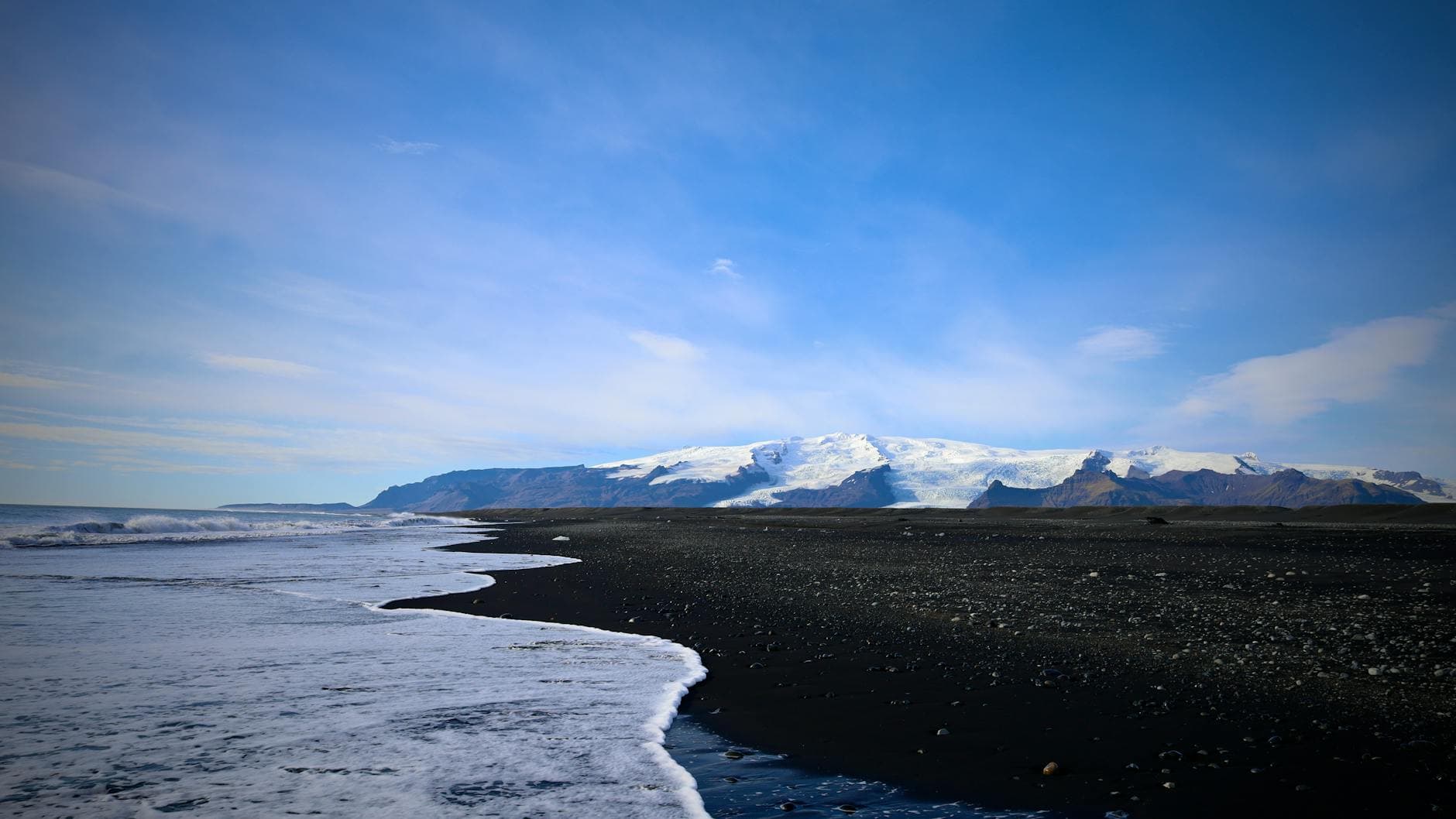 Beautiful view of a black sand beach with snow-capped mountains under a blue sky.