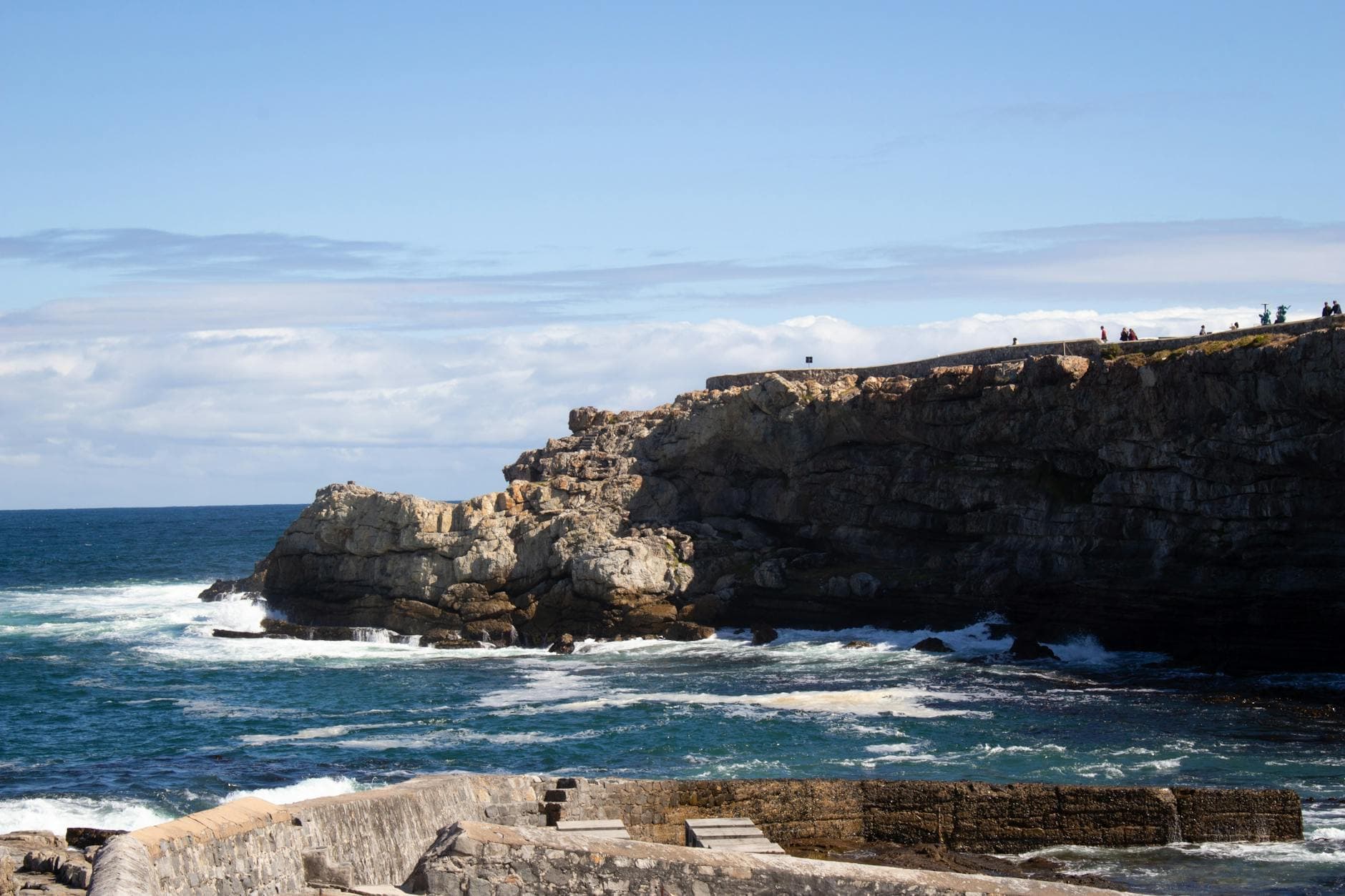 Stunning view of ocean waves crashing against rocky cliffs with people enjoying the scenic landscape.