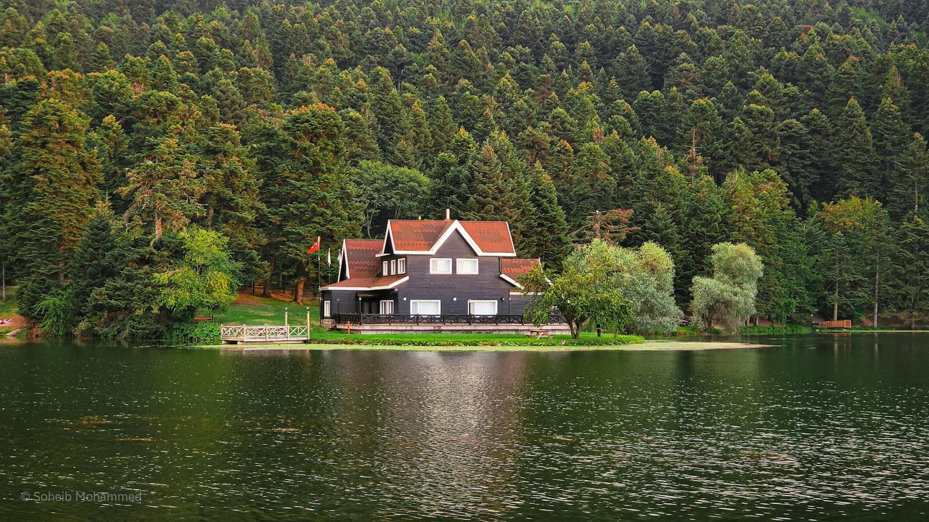 A scenic view of a house by a calm lake surrounded by lush forest in Bolu, Turkey.
