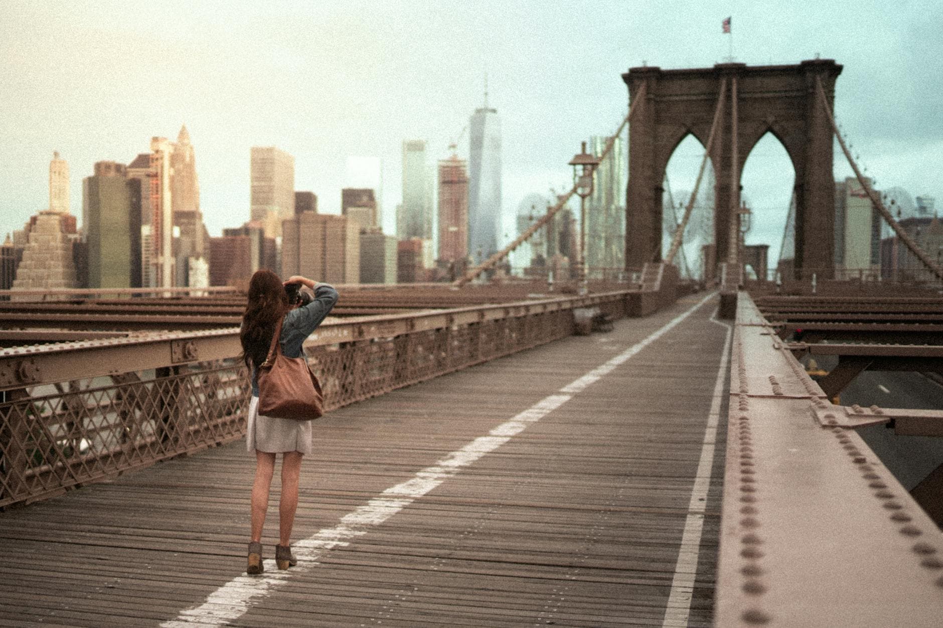 A woman captures the iconic Brooklyn Bridge with the NYC skyline in the background.