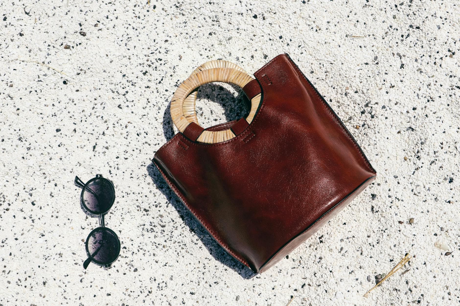 A chic leather bag with sunglasses resting on a sunlit white sand beach in Burdur, Turkey.