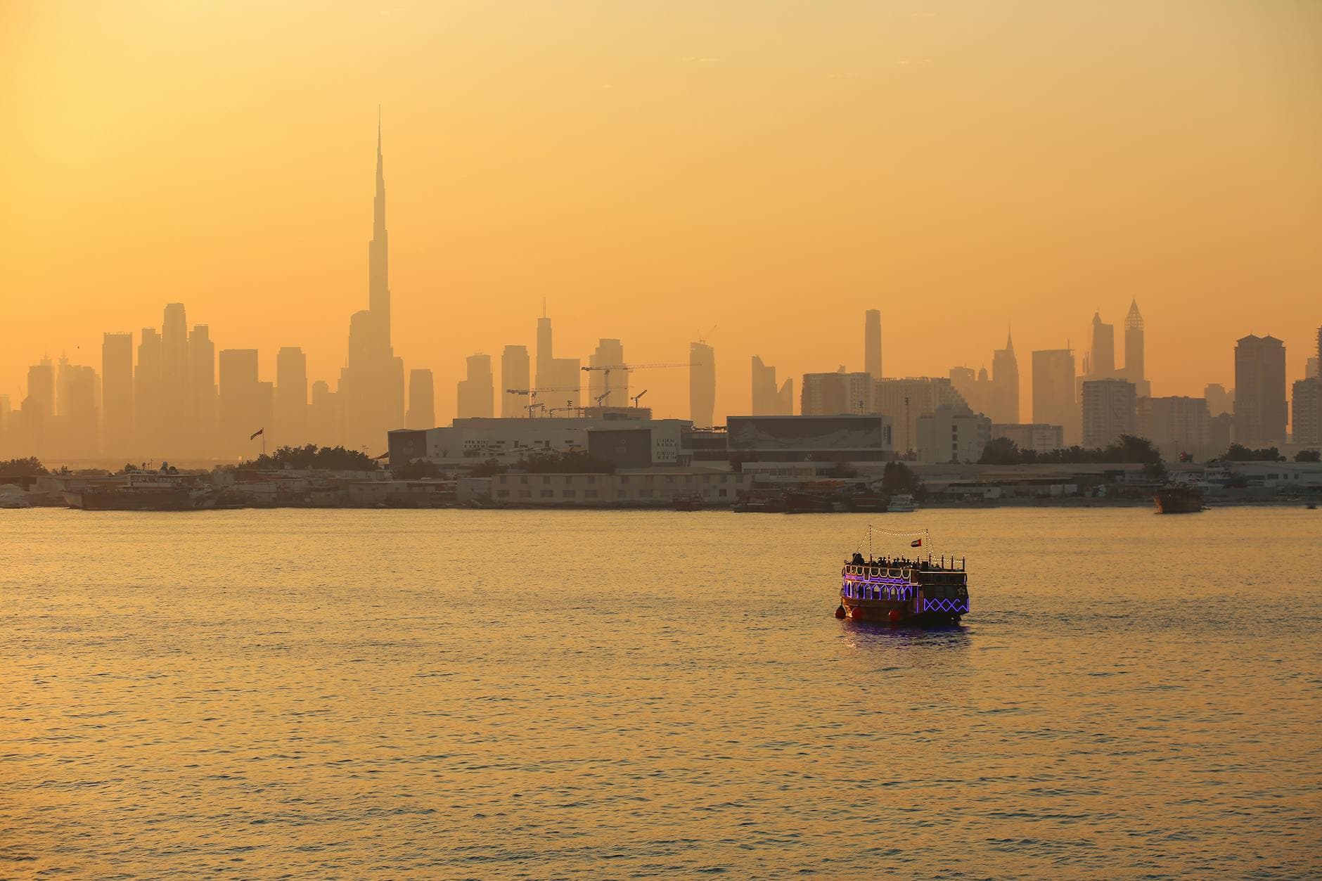 Stunning Dubai skyline with Burj Khalifa during sunset, featuring a lit dhow in the foreground.