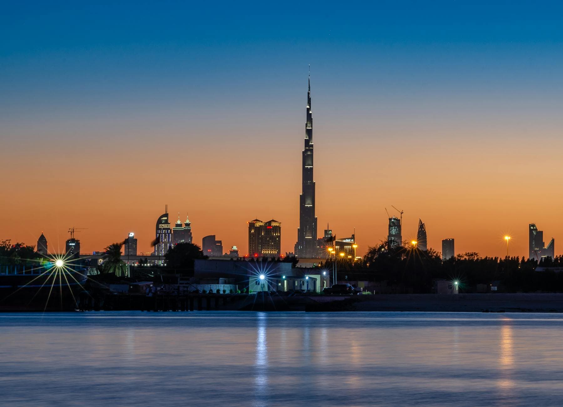 Captivating view of Dubai skyline featuring Burj Khalifa at sunset, reflecting on serene waterfront.