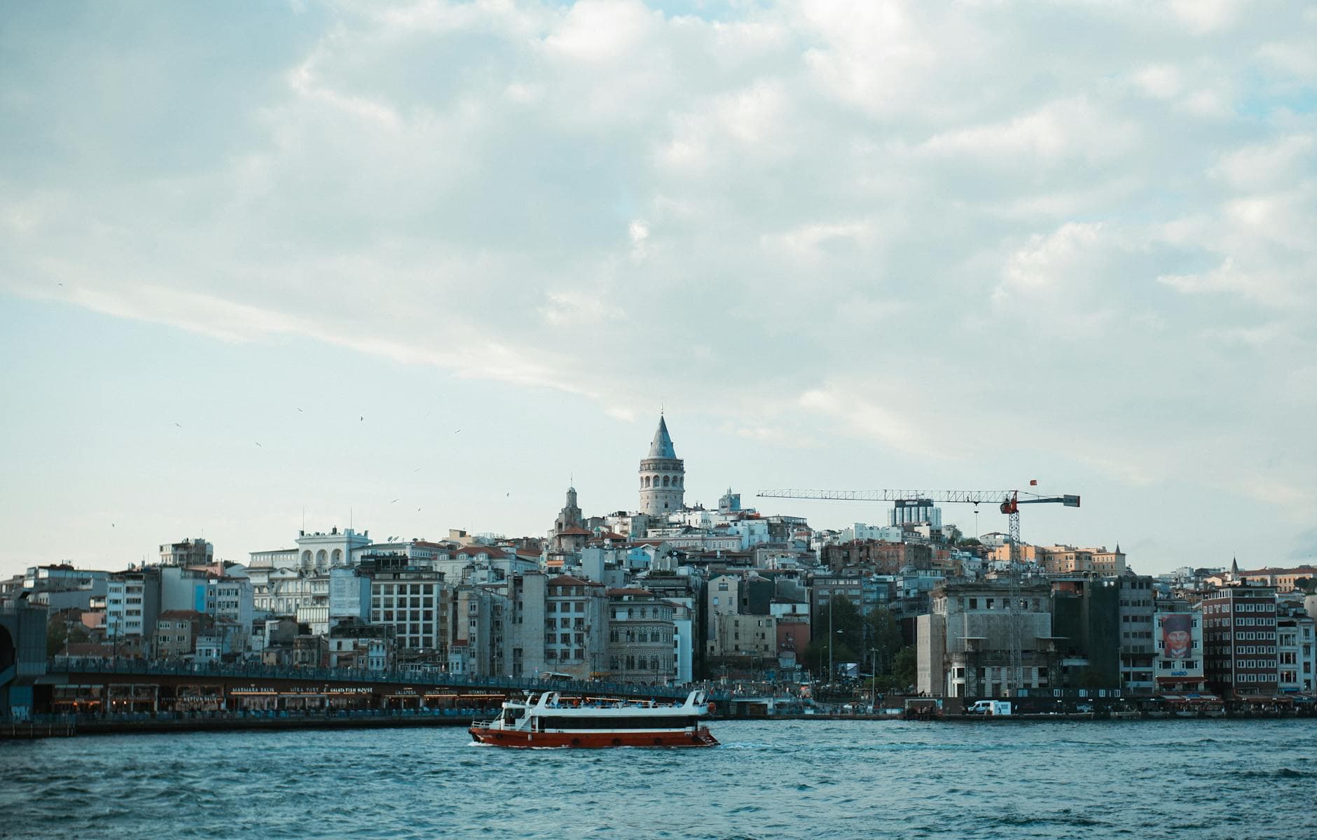 Beautiful view of Istanbul's skyline with Galata Tower and a ferry on the Bosphorus under a cloudy sky.