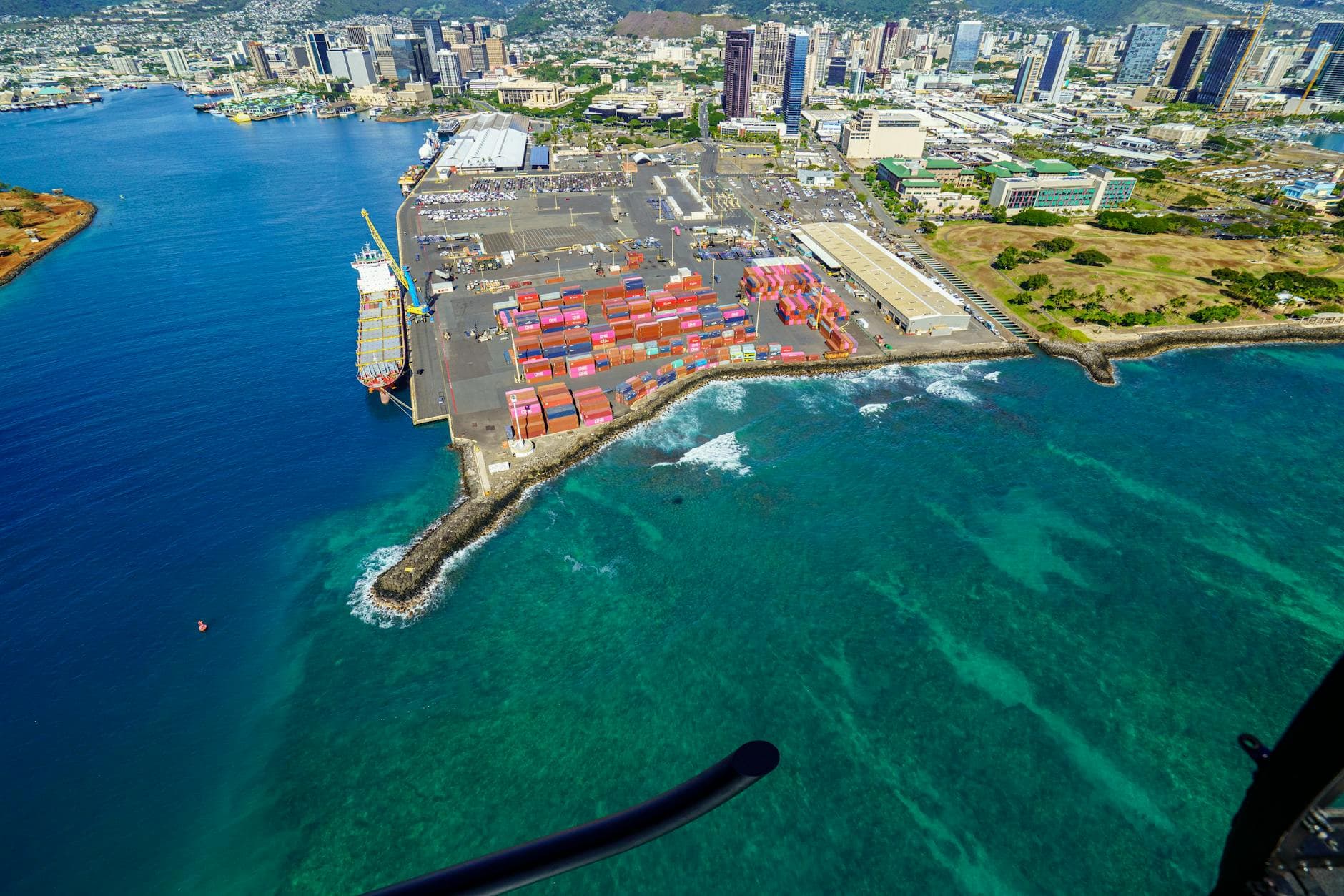 Aerial view of cargo port and cityscape in Honolulu, showcasing vibrant industry and coastal beauty.