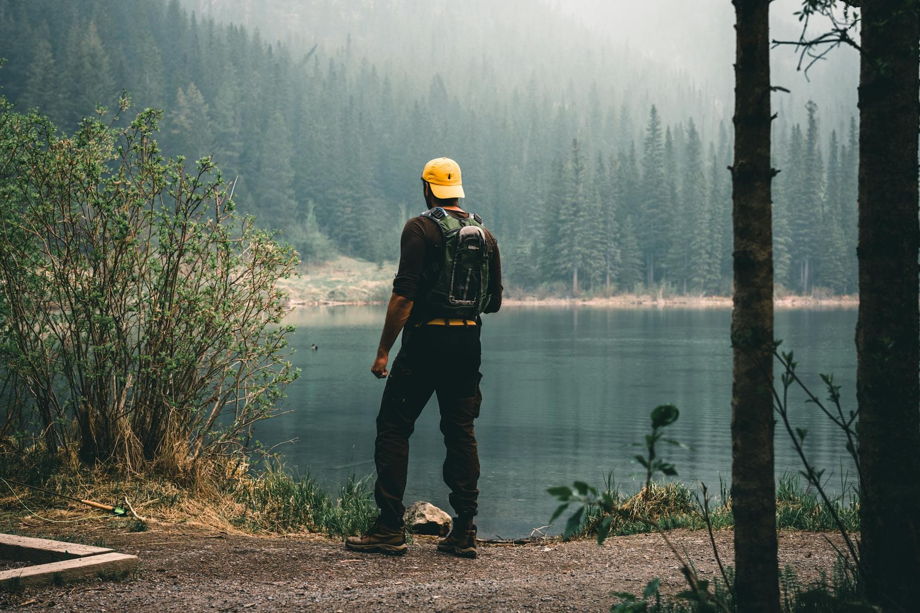 A man stands by a tranquil lake surrounded by a forest in Canmore, Alberta, Canada.