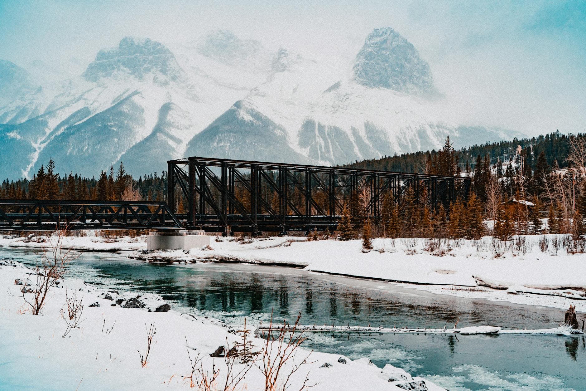 Stunning winter view of a snowy bridge with mountains in Canmore, Alberta.