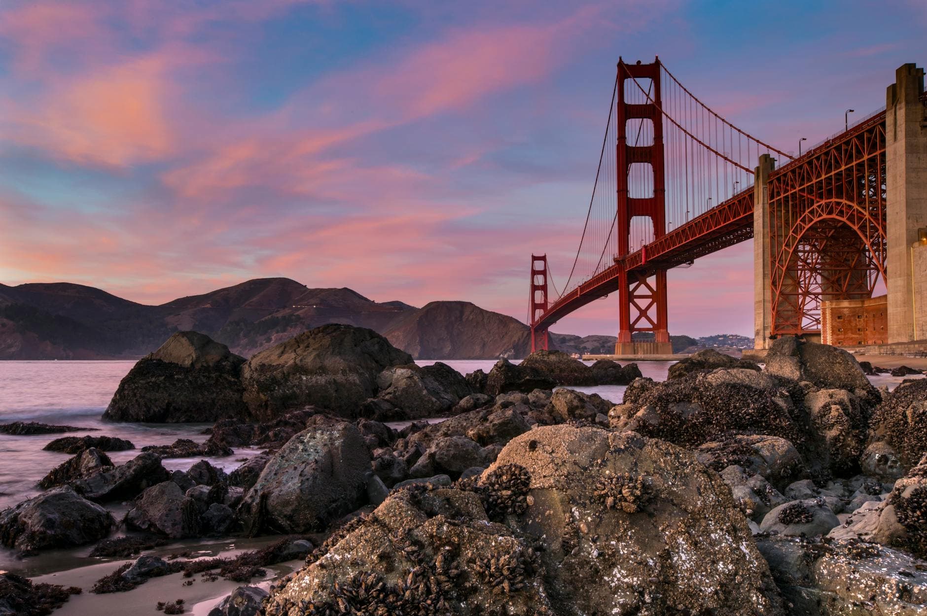 Stunning view of the Golden Gate Bridge at sunset with rocks and ocean foreground.