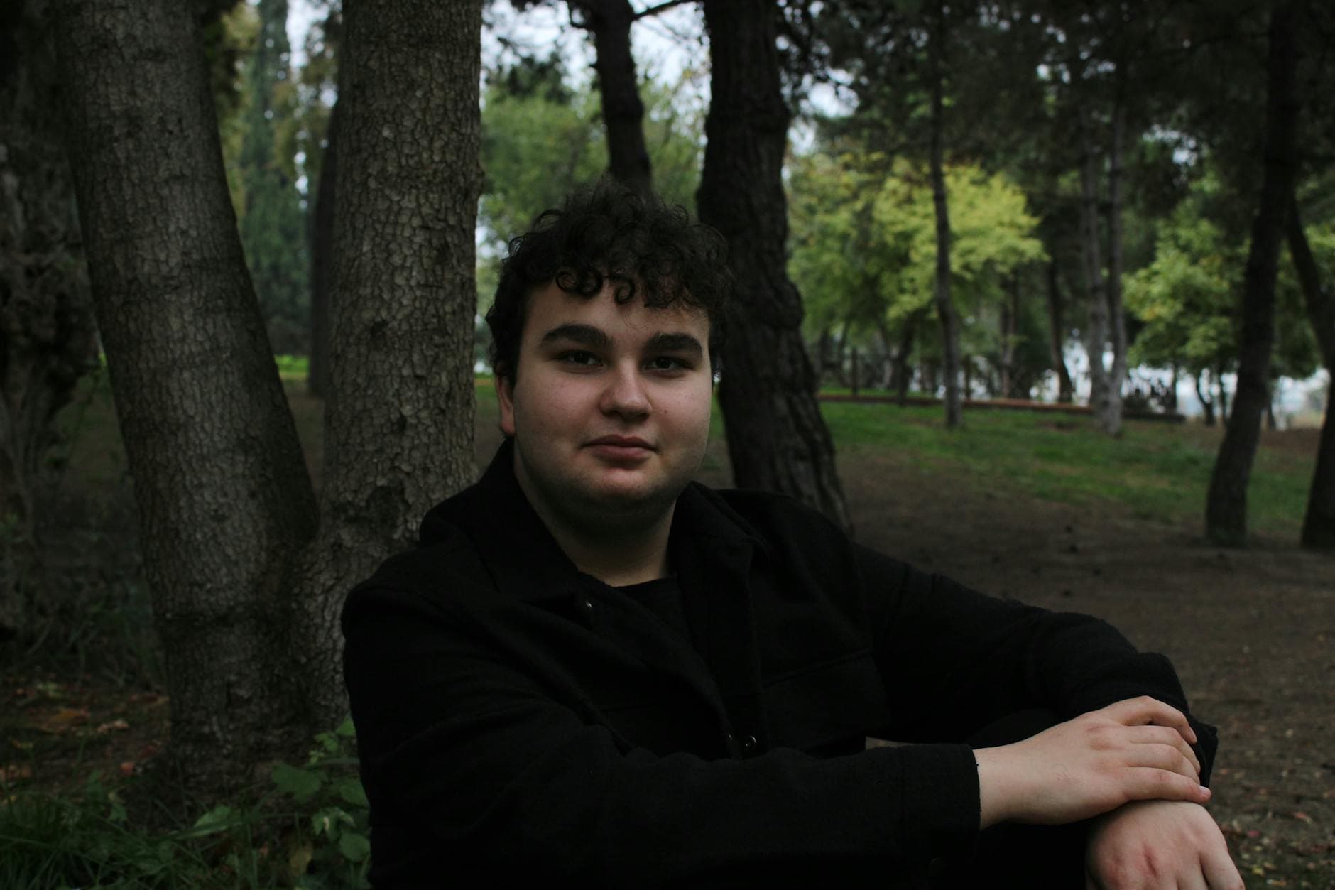 Young man sitting in a lush park setting in Darıca, Kocaeli, Türkiye, surrounded by trees.
