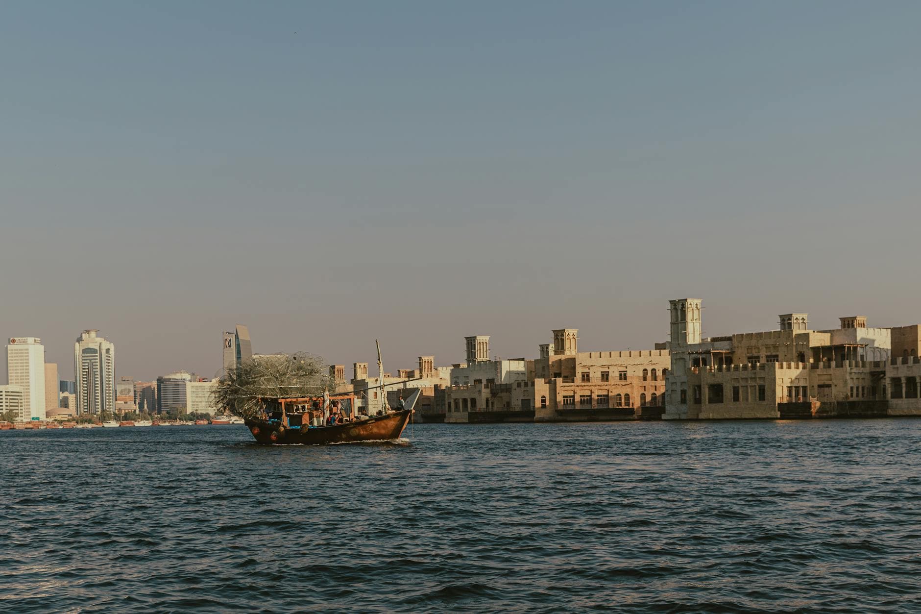 Traditional dhow sailing on Dubai Creek with a backdrop of historic architecture and modern skyscrapers.