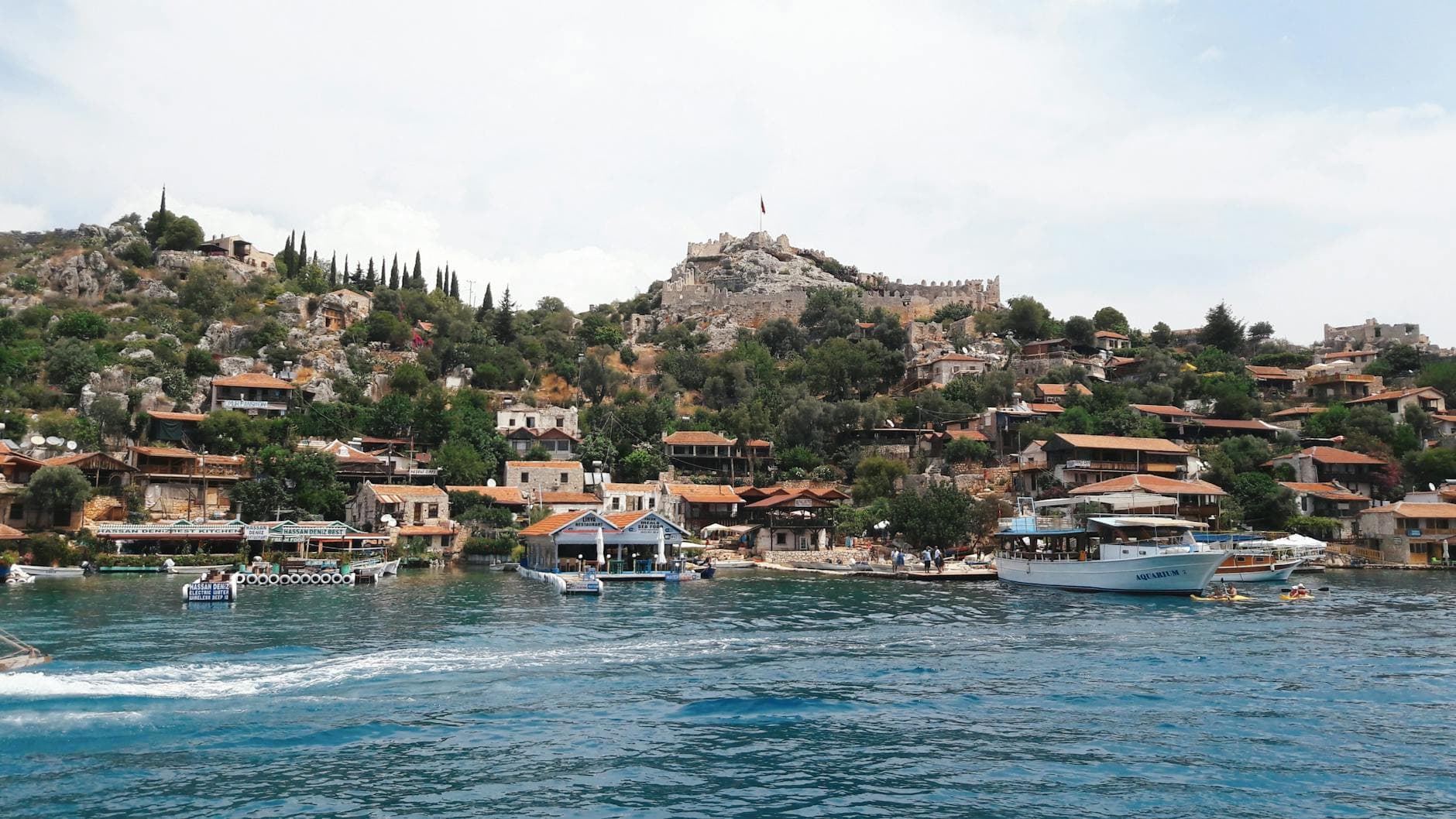 Explore the charming coastal town of Demre, Antalya featuring a hillside castle, vibrant waters, and historic architecture.