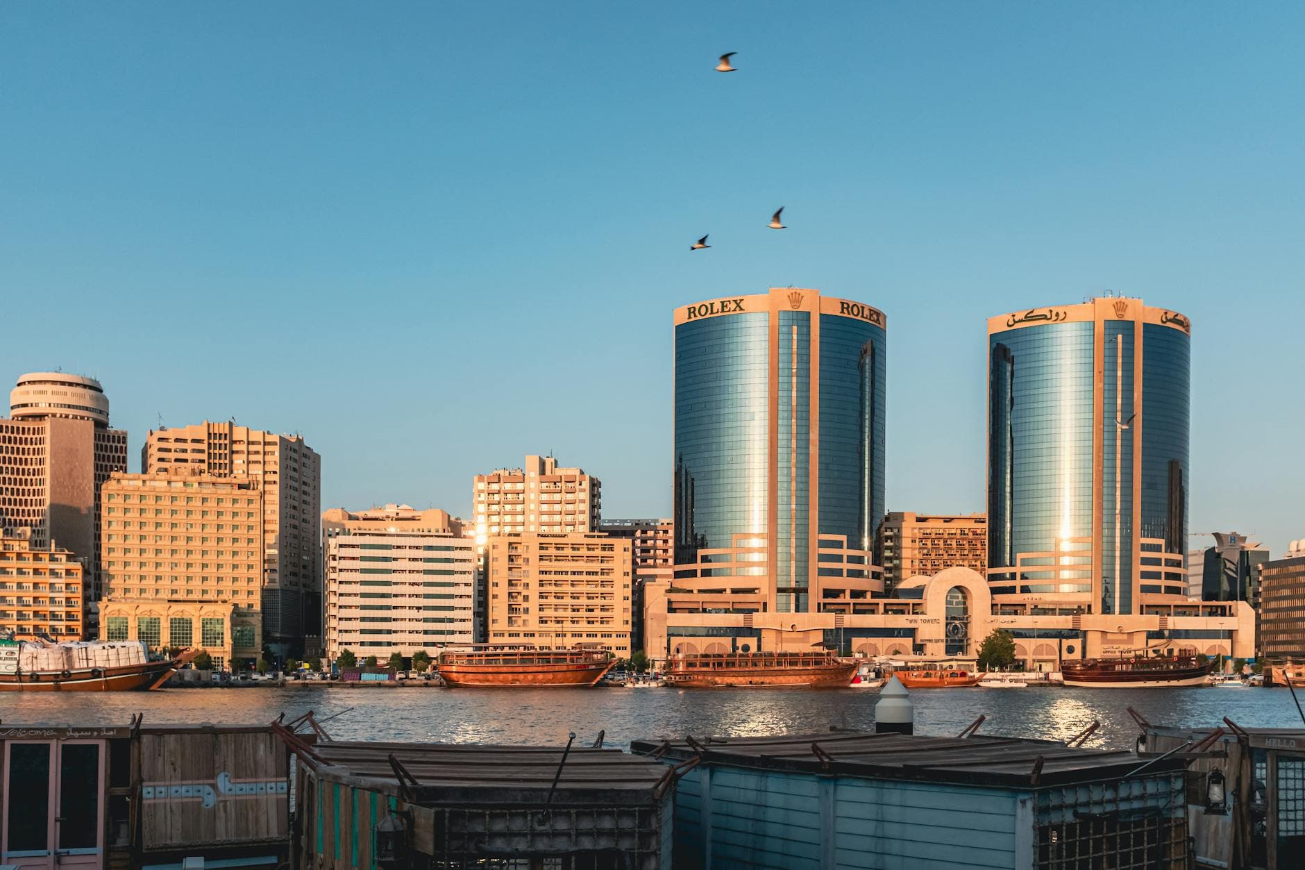 Beautiful sunset view of Dubai Creek with iconic twin towers and traditional boats, capturing the essence of Dubai's waterfront skyline.