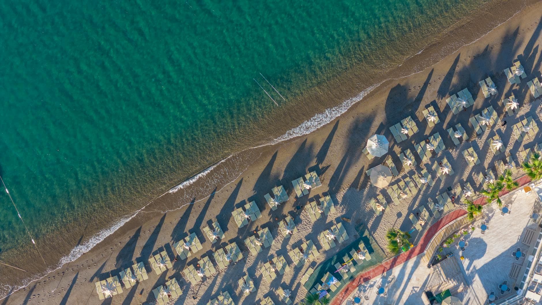 Aerial shot of Bodrum beach in Turkey with sun umbrellas casting shadows.