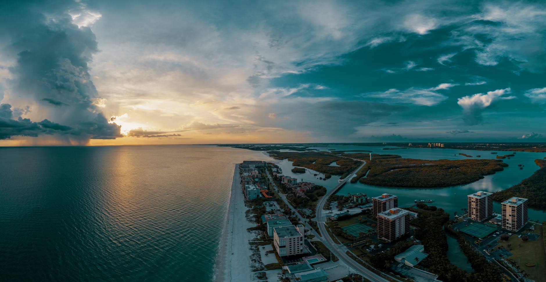 Stunning aerial view of Bonita Springs coastline during sunset with dramatic clouds.