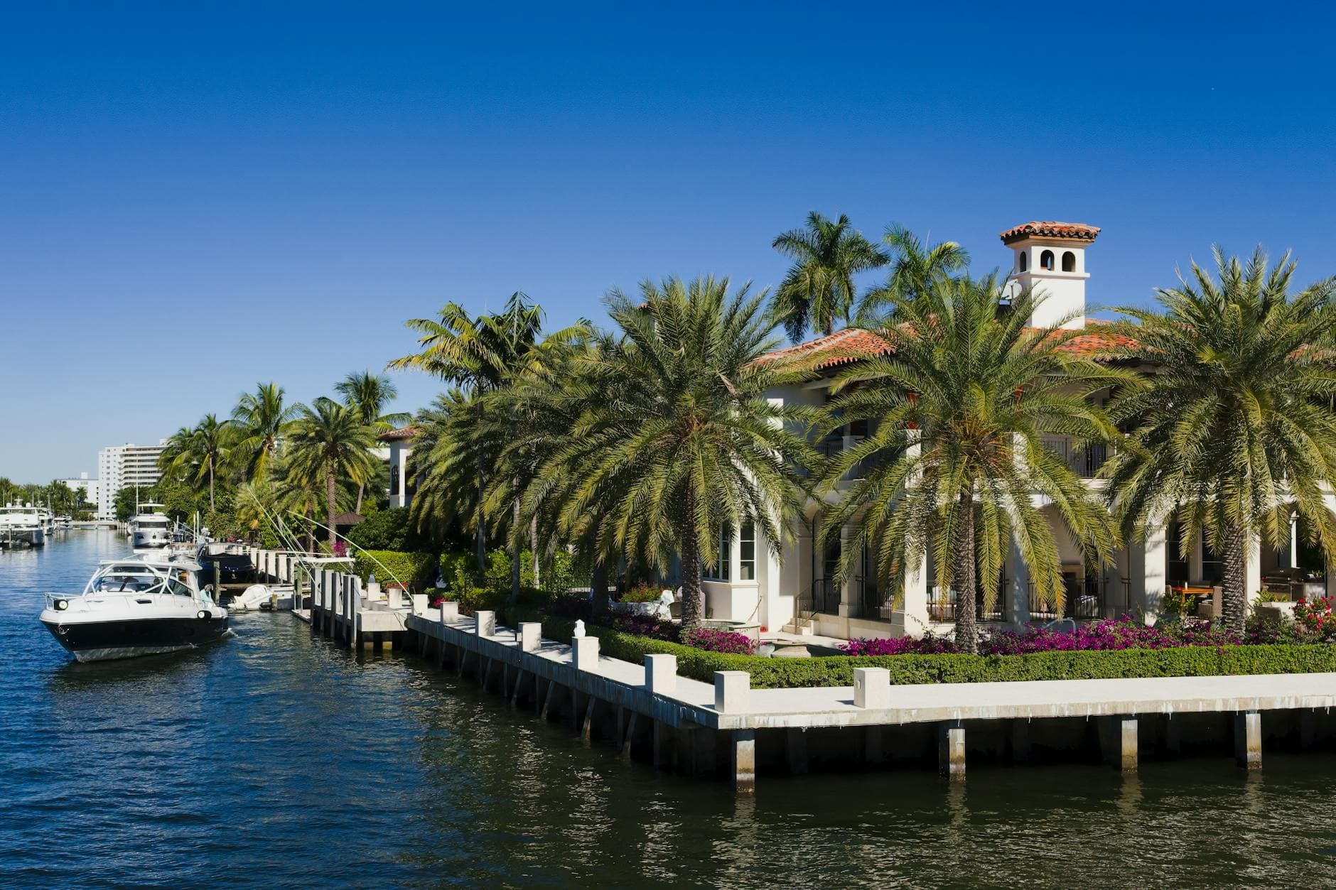 Elegant waterfront mansion with palm trees in Fort Lauderdale, Florida under a clear blue sky.