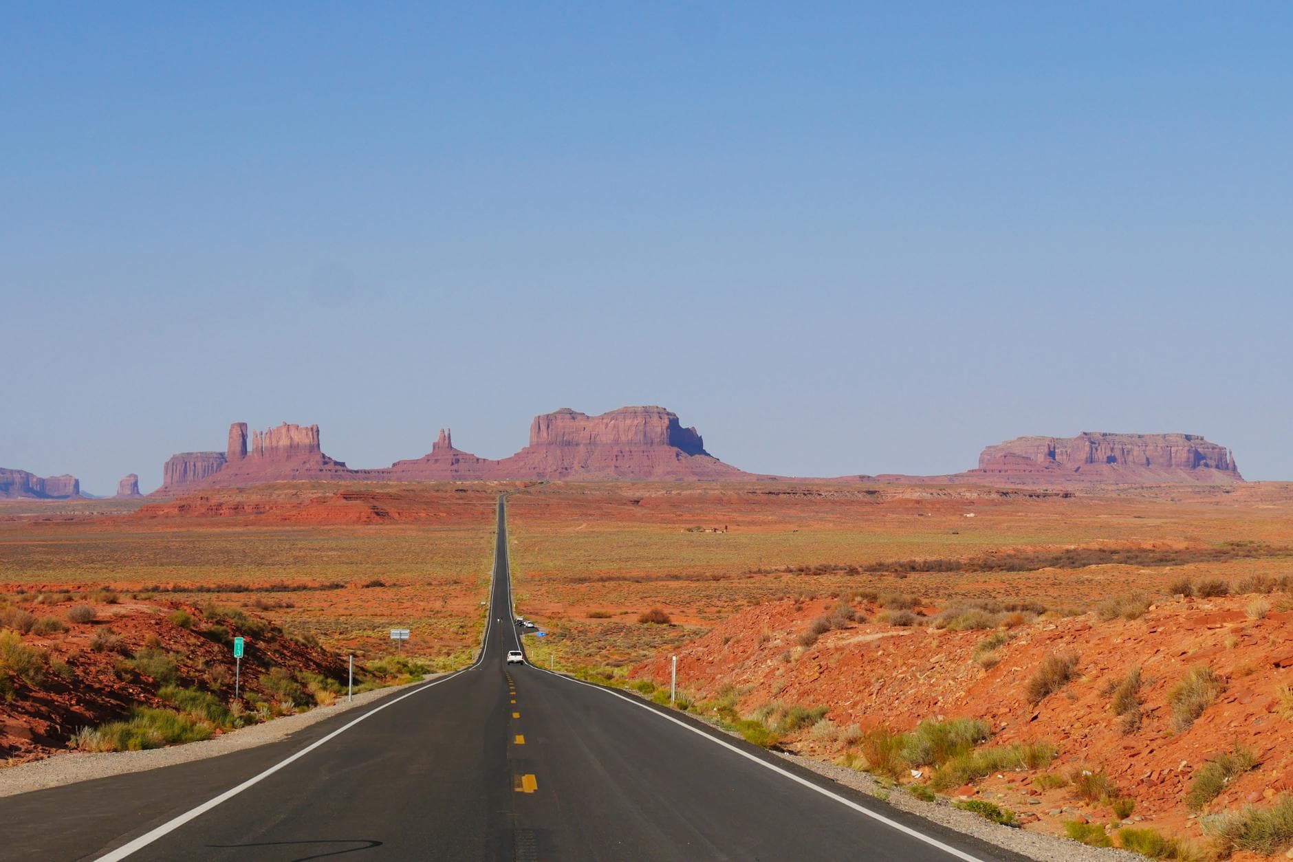 Long straight road through Monument Valley with red rock formations under a clear blue sky.