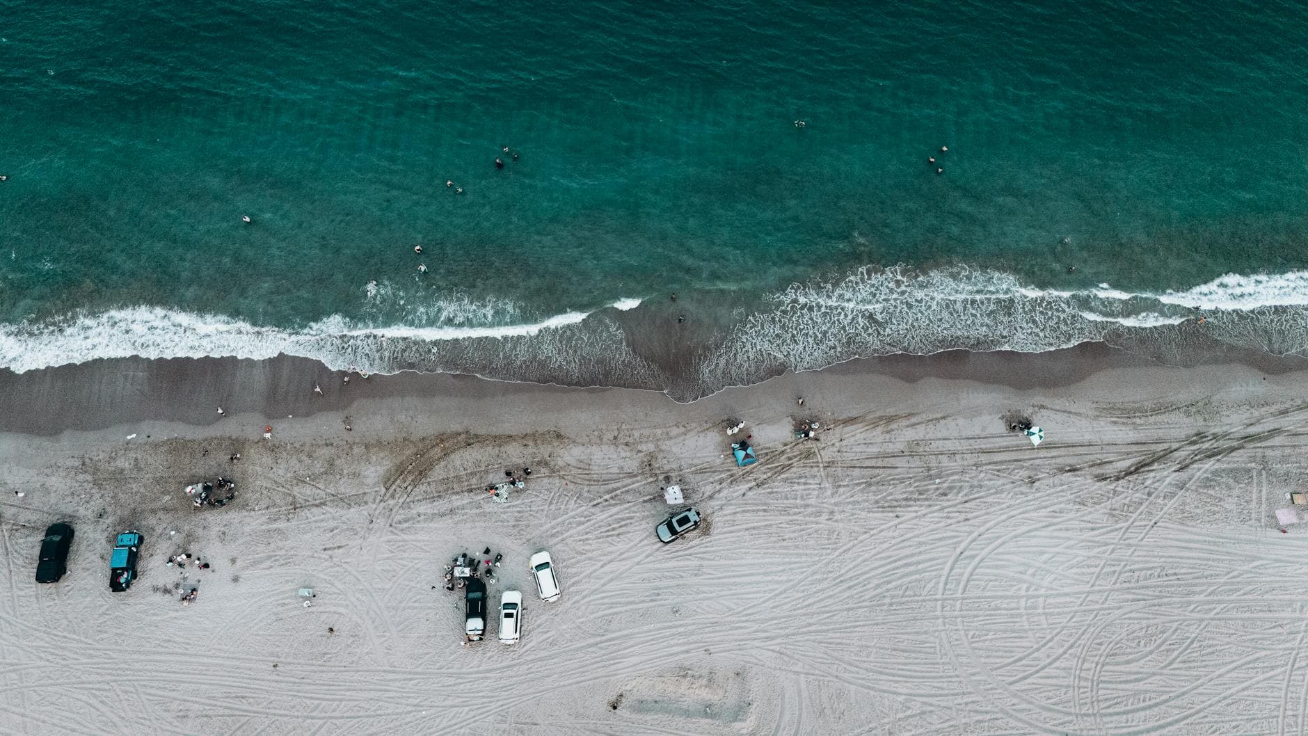A stunning aerial view of Fujairah beach with cars parked along the shoreline and people enjoying the ocean waves.