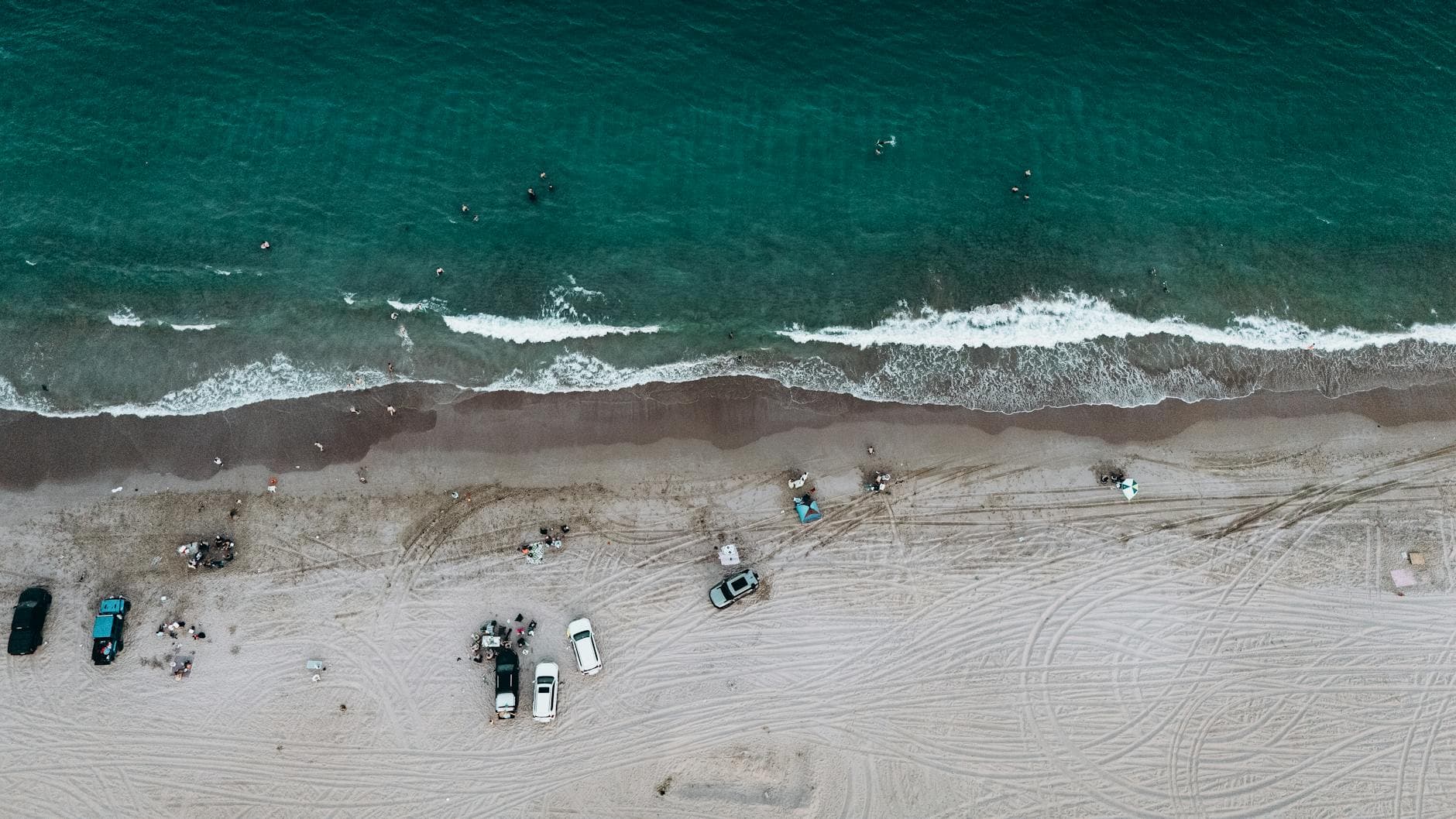 Breathtaking aerial view of Fujairah beach showing parked cars, ocean waves, and beachgoers enjoying the scenery.