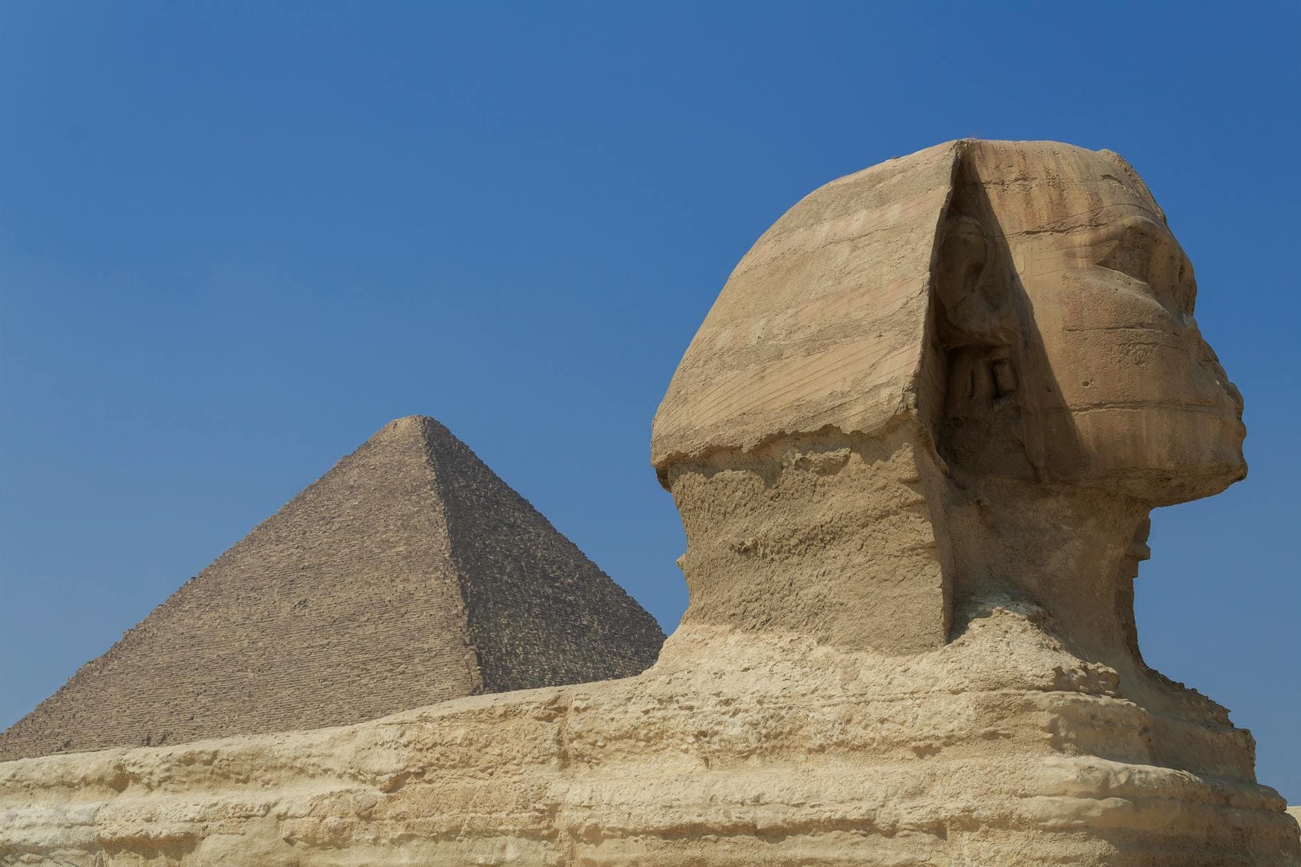 Iconic view of the Great Sphinx with Pyramid of Giza. Historic landmarks in Egypt with clear blue sky.