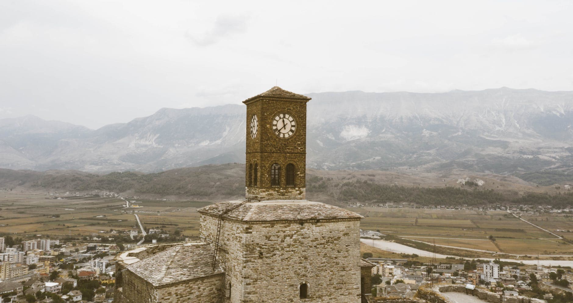 Aerial view of a historical clock tower with scenic mountain backdrop.