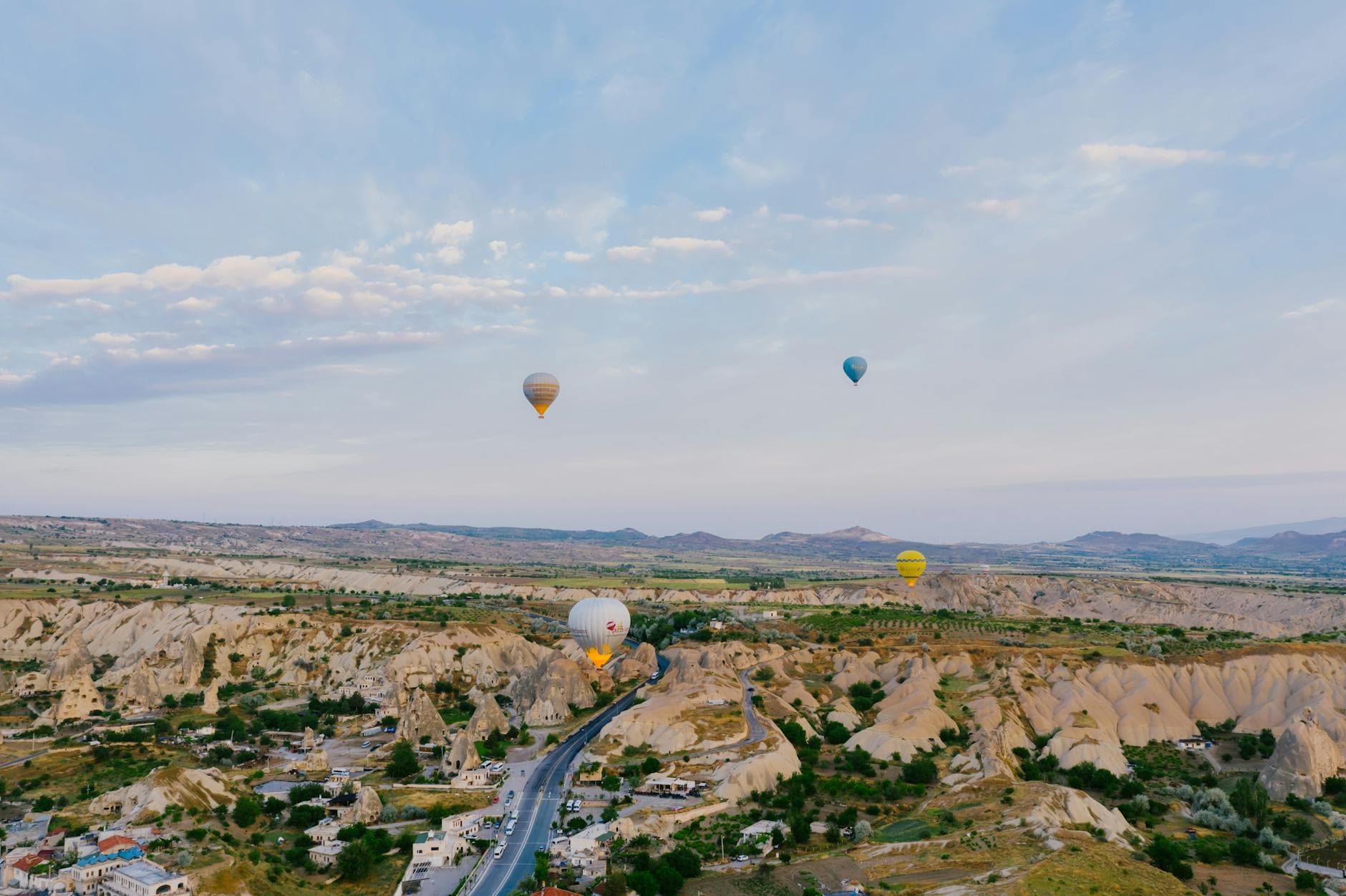 Aerial view of colorful hot air balloons soaring over the rocky landscape and road in Cappadocia, Turkey.
