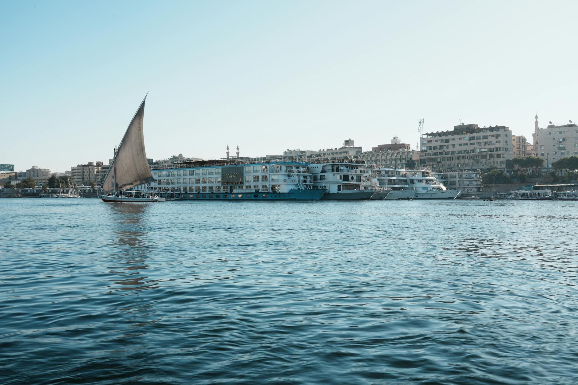 A picturesque view of a traditional sailboat on the Nile River near city waterfronts.