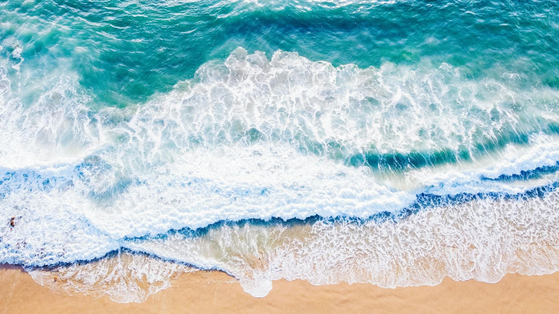 Stunning aerial shot of waves crashing on Hermosa Beach, showcasing its turquoise waters and smooth sand.