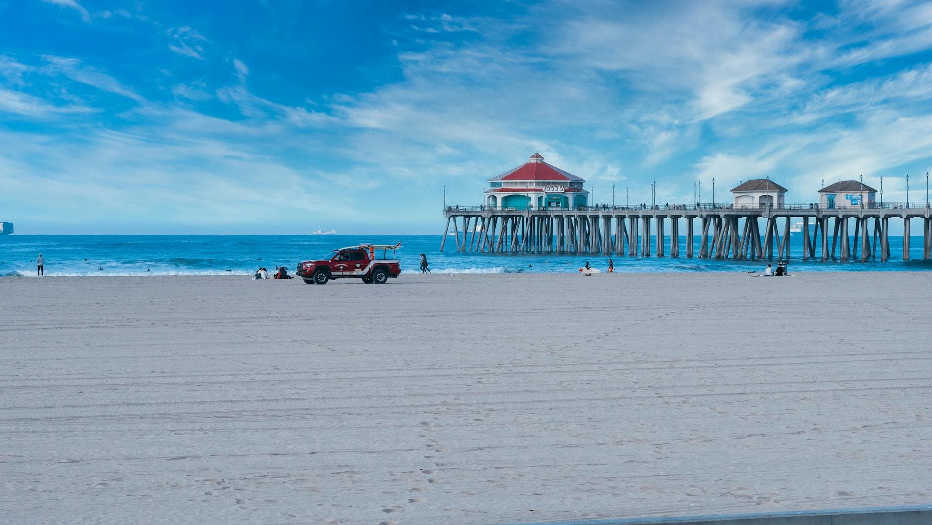 Serene view of Huntington Beach Pier with lifeguard vehicle and visitors enjoying the sunny coastline.