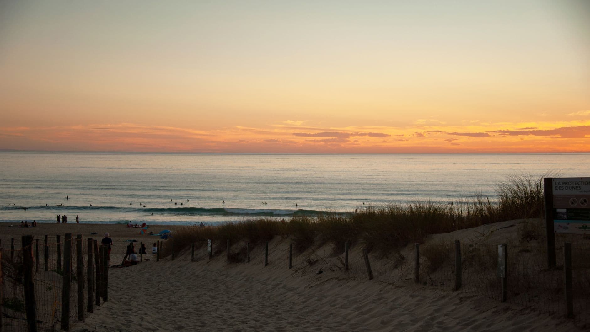 Beautiful sunset over Seignosse Beach with surfers enjoying the waves and stunning horizon views.