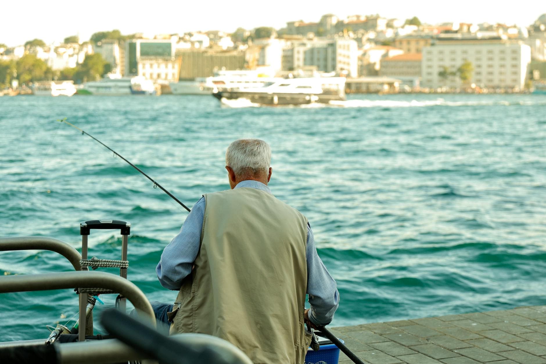 Senior man fishing by the Bosphorus with a city skyline in the background, Istanbul.