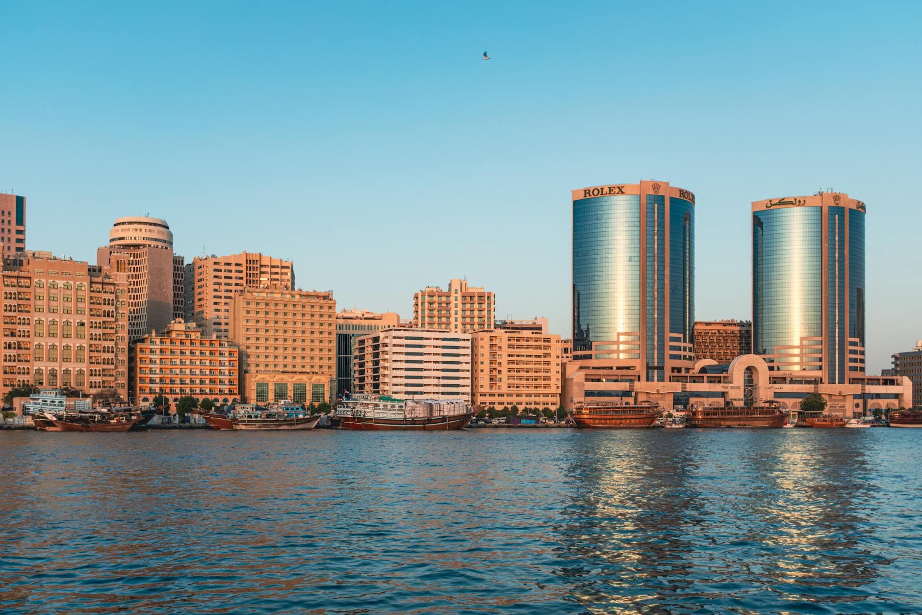 Scenic view of Dubai's Deira Twin Towers and waterfront during sunset, showcasing modern architecture and vibrant urban life.